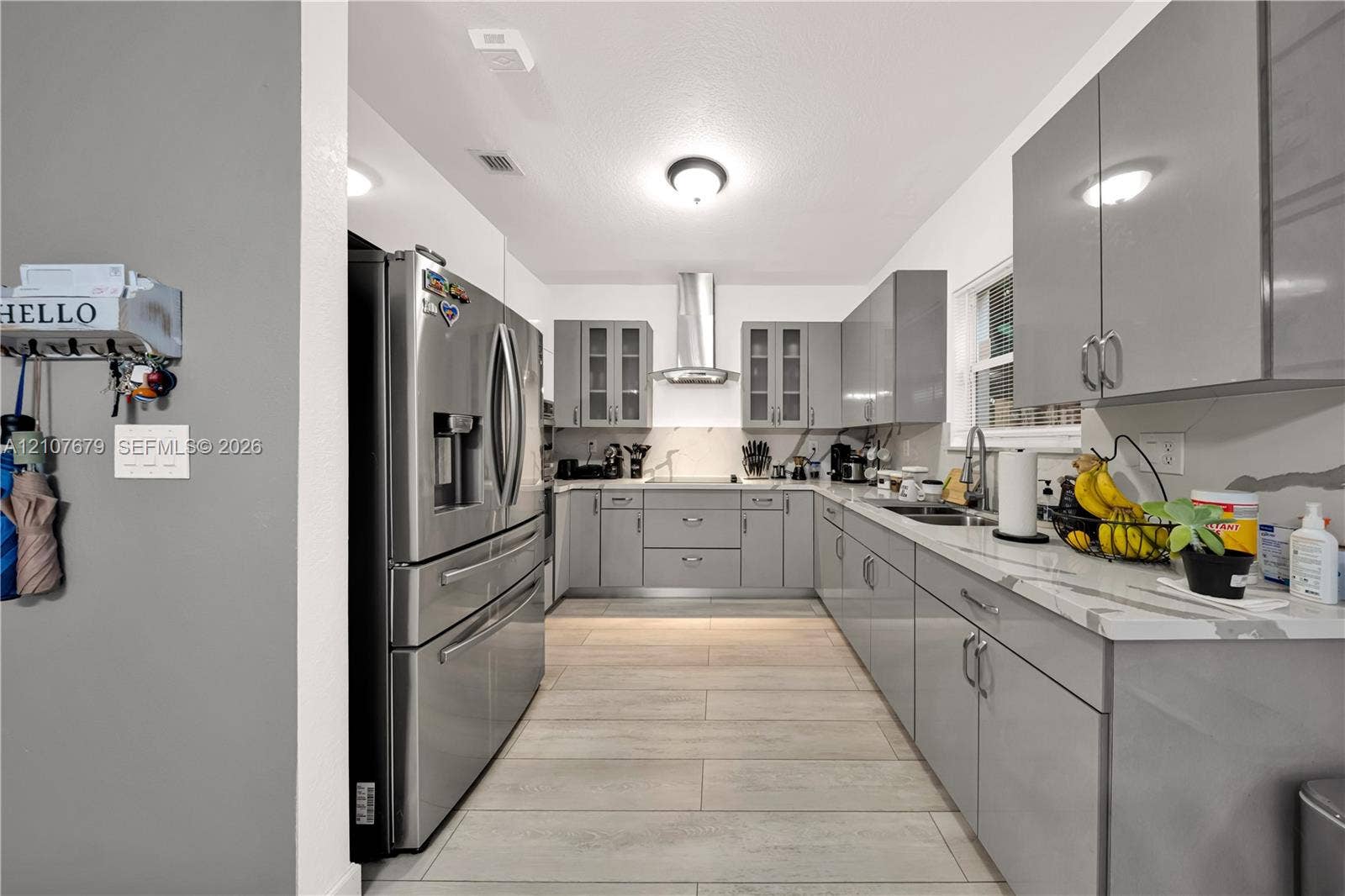 22066 SW 93rd Place, Cutler Bay, FL 33190 Kitchen featuring high-gloss grey cabinetry, stainless steel appliances, quartz countertops, a modern chimney-style range hood, and tile flooring