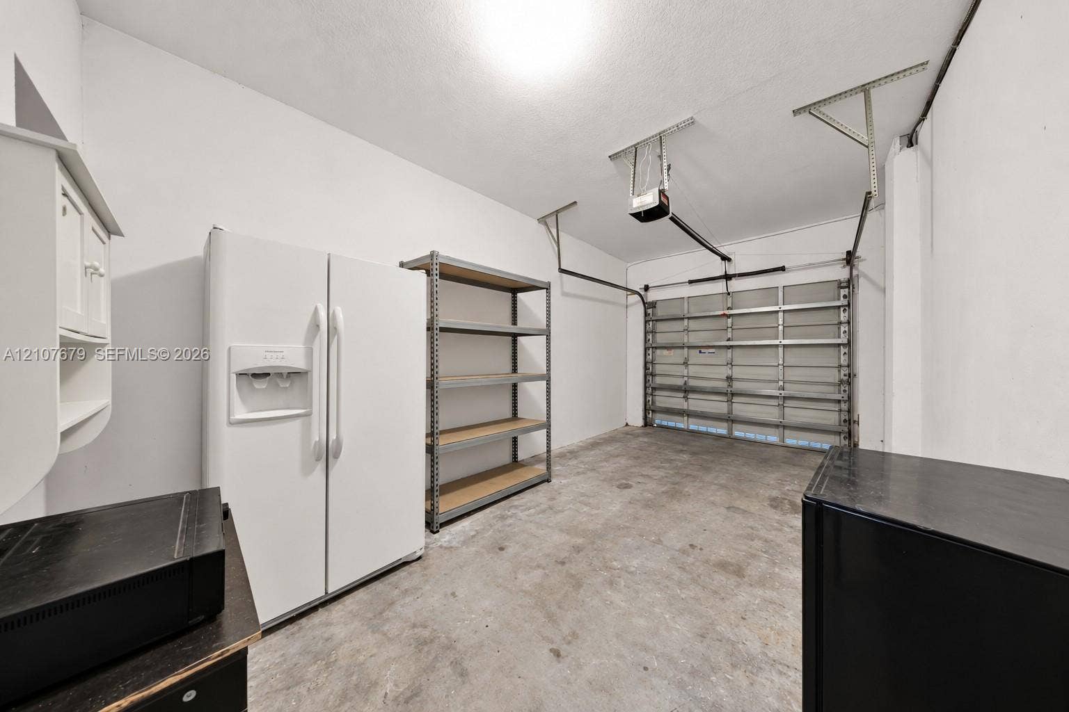 22066 SW 93rd Place, Cutler Bay, FL 33190 Garage space featuring an automatic overhead door opener, concrete flooring, and built-in wall-mounted cabinetry