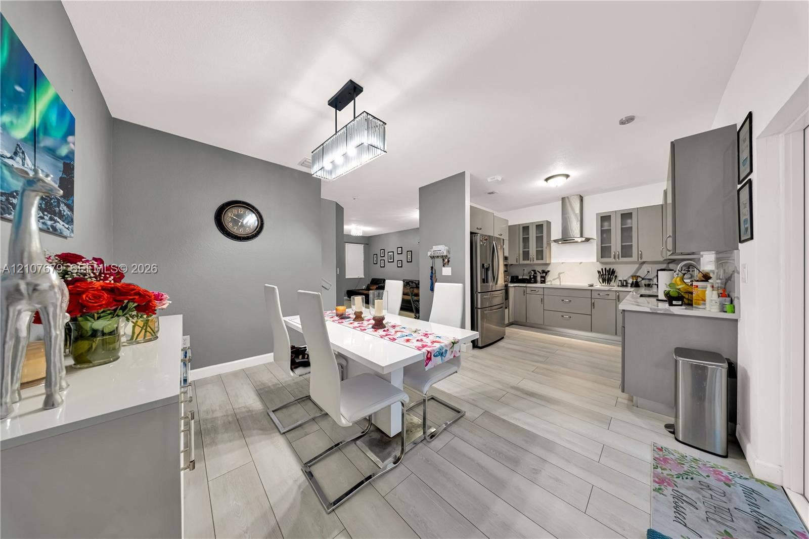 22066 SW 93rd Place, Cutler Bay, FL 33190 Open-concept kitchen and dining area featuring wood-finish plank flooring, gray shaker-style cabinetry, stone countertops, a stainless steel range hood, and a modern rectangular pendant light fixture