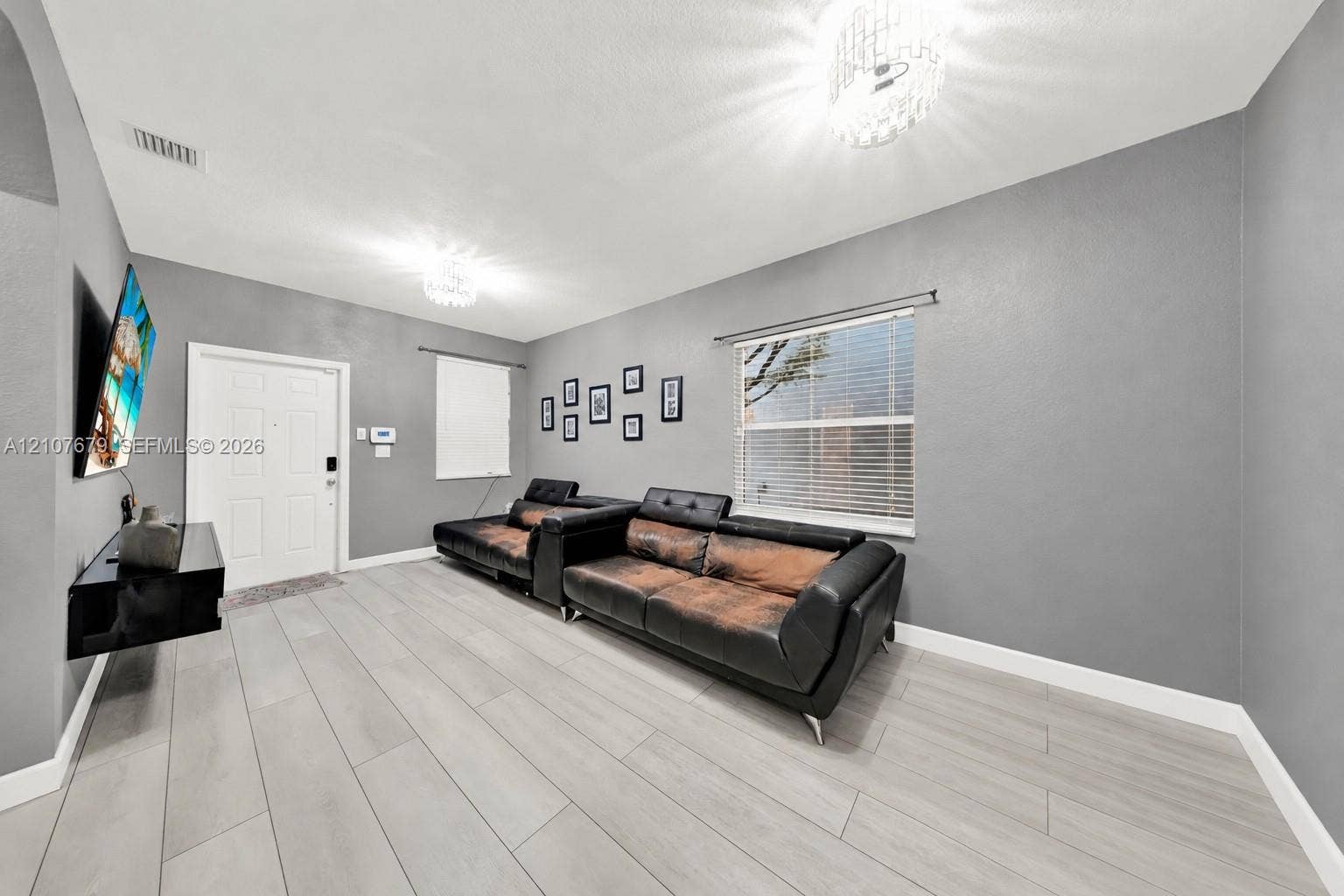 22066 SW 93rd Place, Cutler Bay, FL 33190 Interior space featuring wood-finish flooring, neutral gray wall paint, dual crystal-style chandeliers, and a white paneled entry door