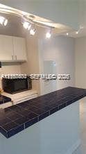 6310 SW 79th Street, #12, South Miami, South Miami, FL 33143 Kitchen featuring a dark tile-surfaced breakfast bar, white cabinetry, track lighting, and a built-in microwave