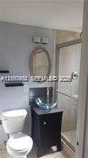 6310 SW 79th Street, #12, South Miami, South Miami, FL 33143 Bathroom featuring a dark wood vanity with a glass vessel sink, oval wall-mounted mirror, two floating wall shelves, and a walk-in shower with a glass enclosure