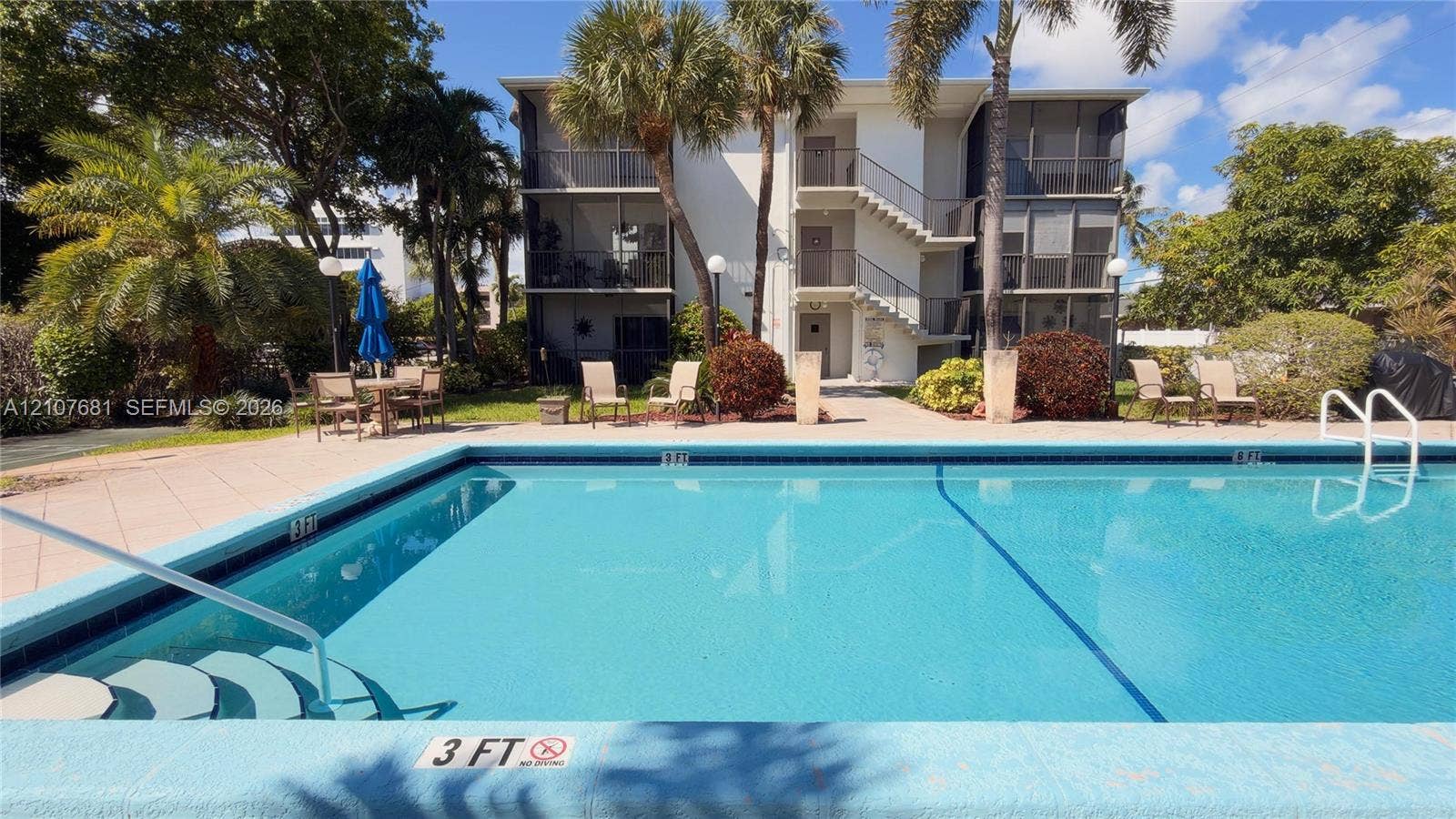 701 NE 1st Court, #202, Hallandale Beach, Hallandale Beach, FL 33009 In-ground swimming pool featuring a tiled deck, stair entry, and metal handrails, set against a multi-story exterior with screened balconies