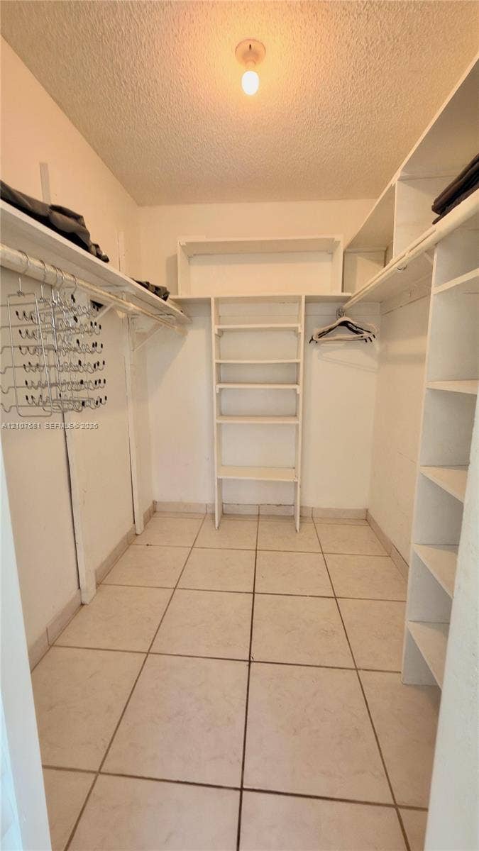 701 NE 1st Court, #202, Hallandale Beach, Hallandale Beach, FL 33009 Walk-in closet featuring large-format tile flooring, built-in white shelving units, overhead hanging rods, and ceiling-mounted lighting