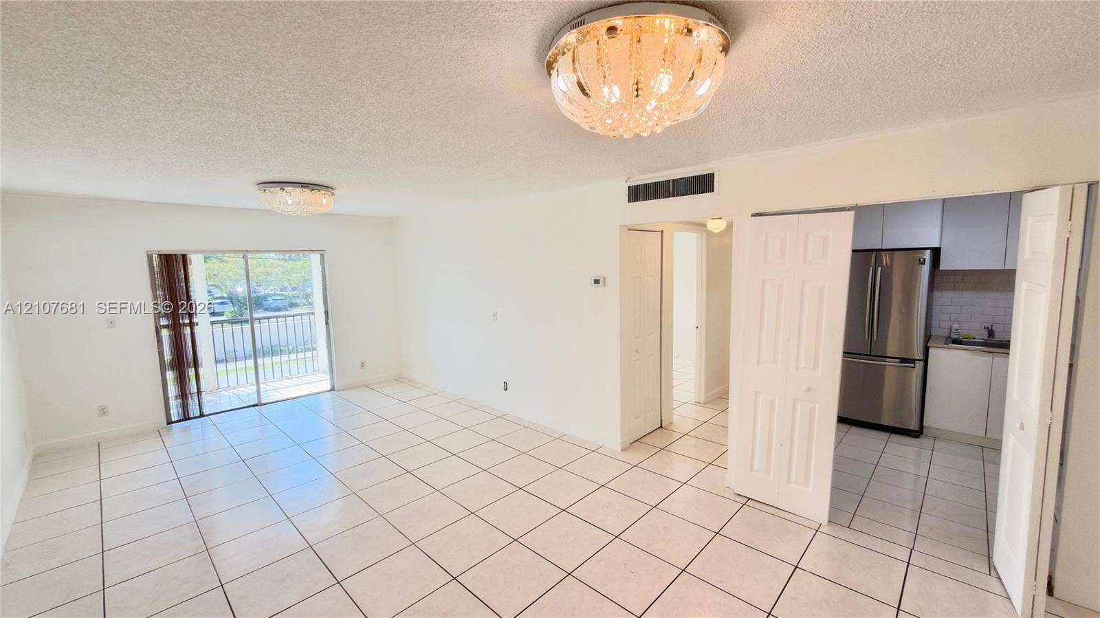 701 NE 1st Court, #202, Hallandale Beach, Hallandale Beach, FL 33009 Open-concept area featuring white ceramic tile flooring, crystal-style flush-mount ceiling light fixtures, sliding glass doors with balcony access, and a kitchen equipped with stainless steel appliances