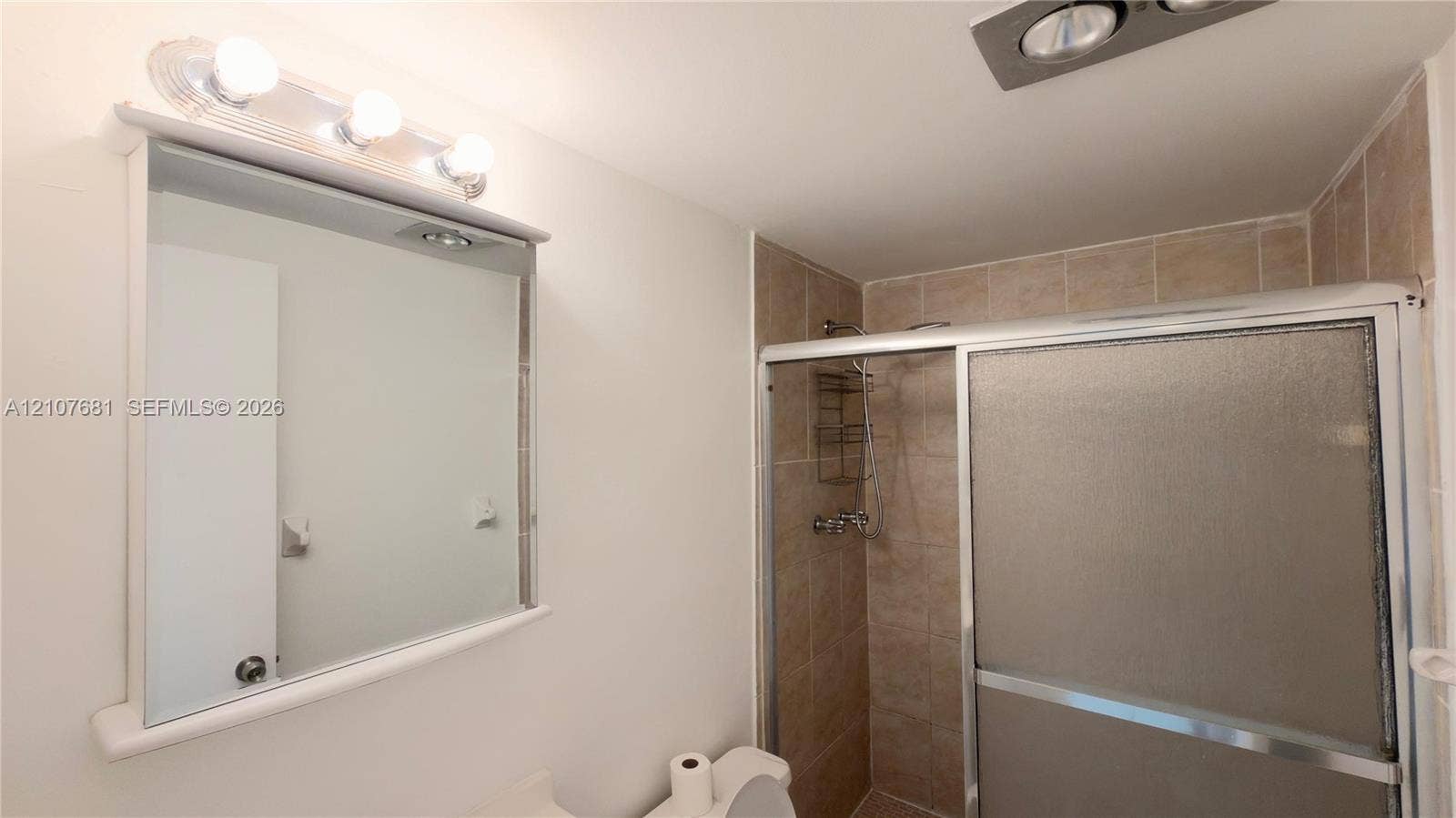 701 NE 1st Court, #202, Hallandale Beach, Hallandale Beach, FL 33009 Bathroom featuring a shower stall with sliding glass doors, neutral-toned tiled walls, a wall-mounted vanity mirror with a three-bulb light fixture, and an integrated ceiling exhaust fan
