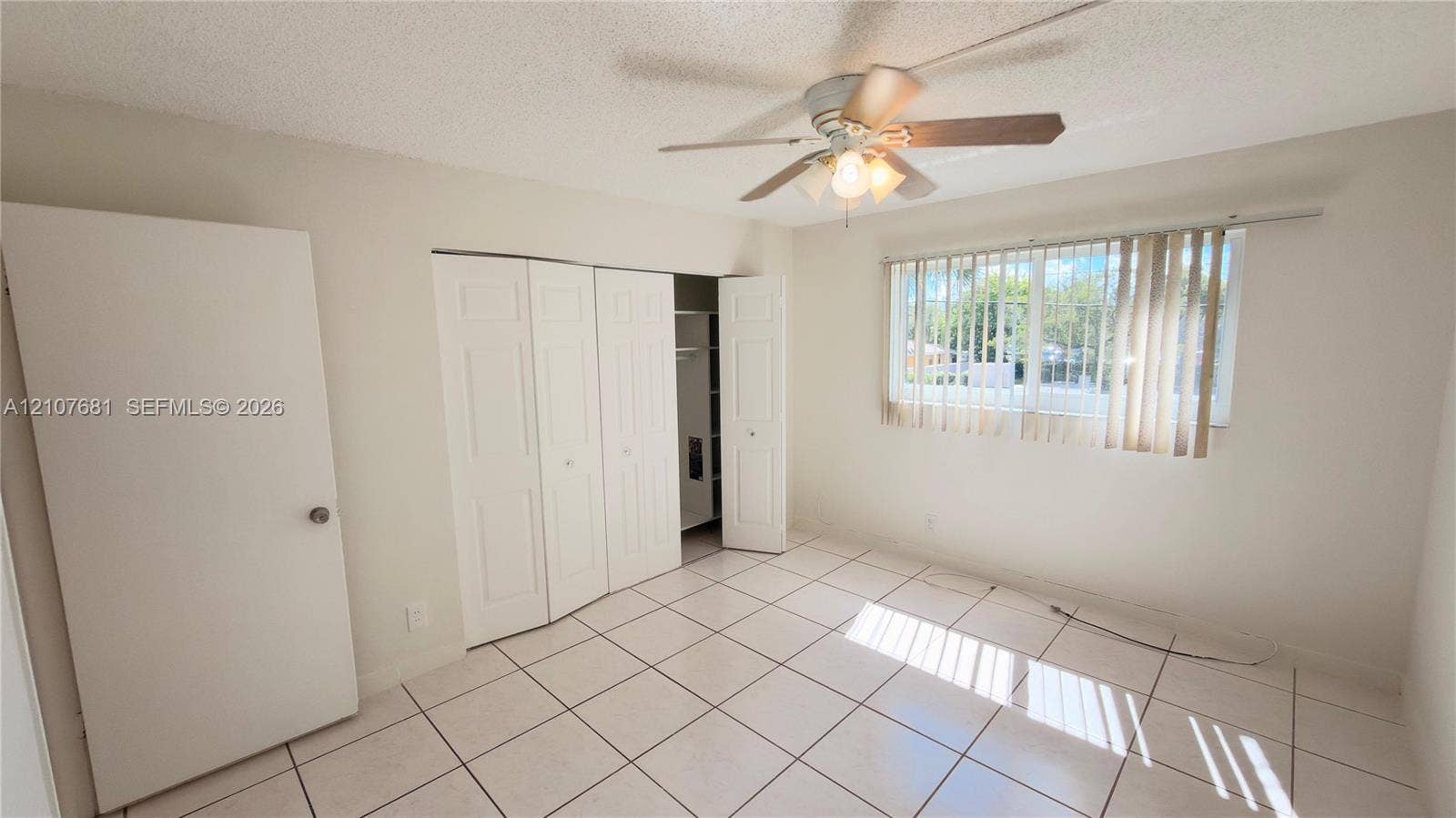 701 NE 1st Court, #202, Hallandale Beach, Hallandale Beach, FL 33009 Room featuring white tile flooring, multi-panel bi-fold closet doors, ceiling fan with integrated lighting, and vertical window blinds
