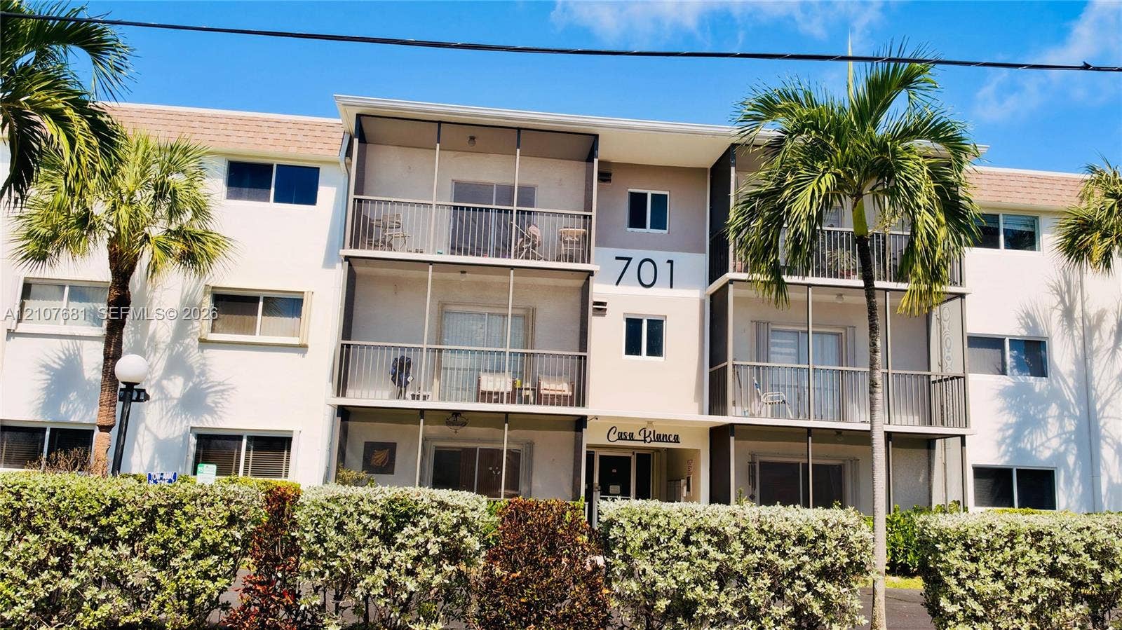701 NE 1st Court, #202, Hallandale Beach, Hallandale Beach, FL 33009 Multi-story stucco exterior featuring screened balconies, covered ground-level entry, and mature perimeter landscaping