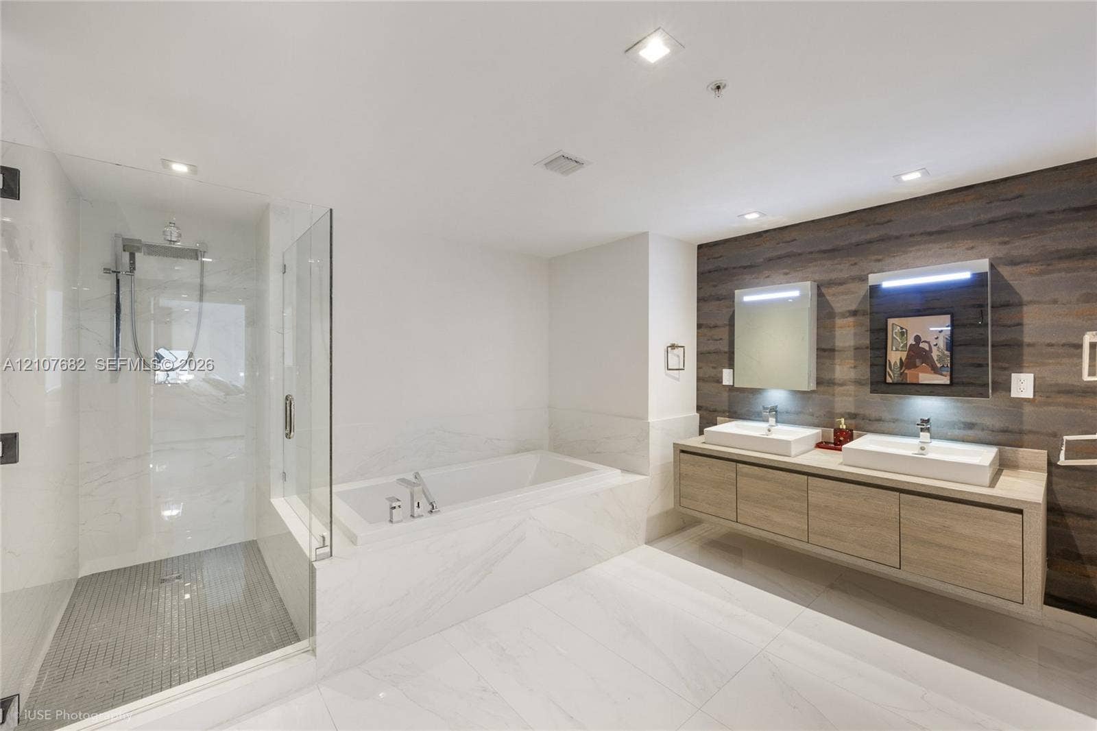 400 Sunny Isles Boulevard, #704, Sunny Isles Beach, Sunny Isles Beach, FL 33160 Floating dual-sink vanity with countertop, wood-finish wall paneling, glass-enclosed walk-in shower with tile flooring, and integrated soaking tub featuring stone-finish surrounds