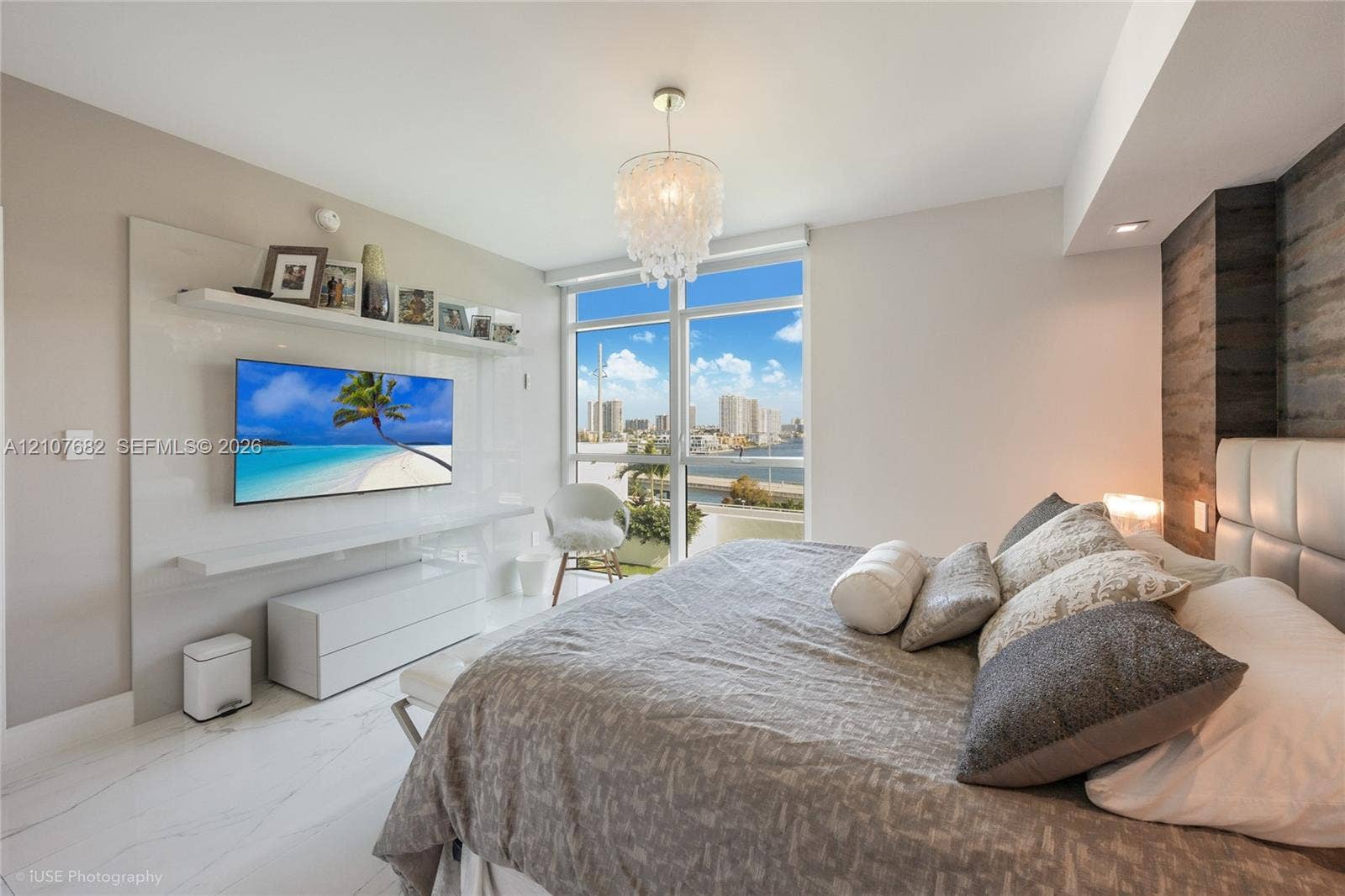 400 Sunny Isles Boulevard, #704, Sunny Isles Beach, Sunny Isles Beach, FL 33160 Floor-to-ceiling windows, custom built-in white media console with integrated shelving, wood-finish accent wall, polished stone-finish flooring, and decorative chandelier