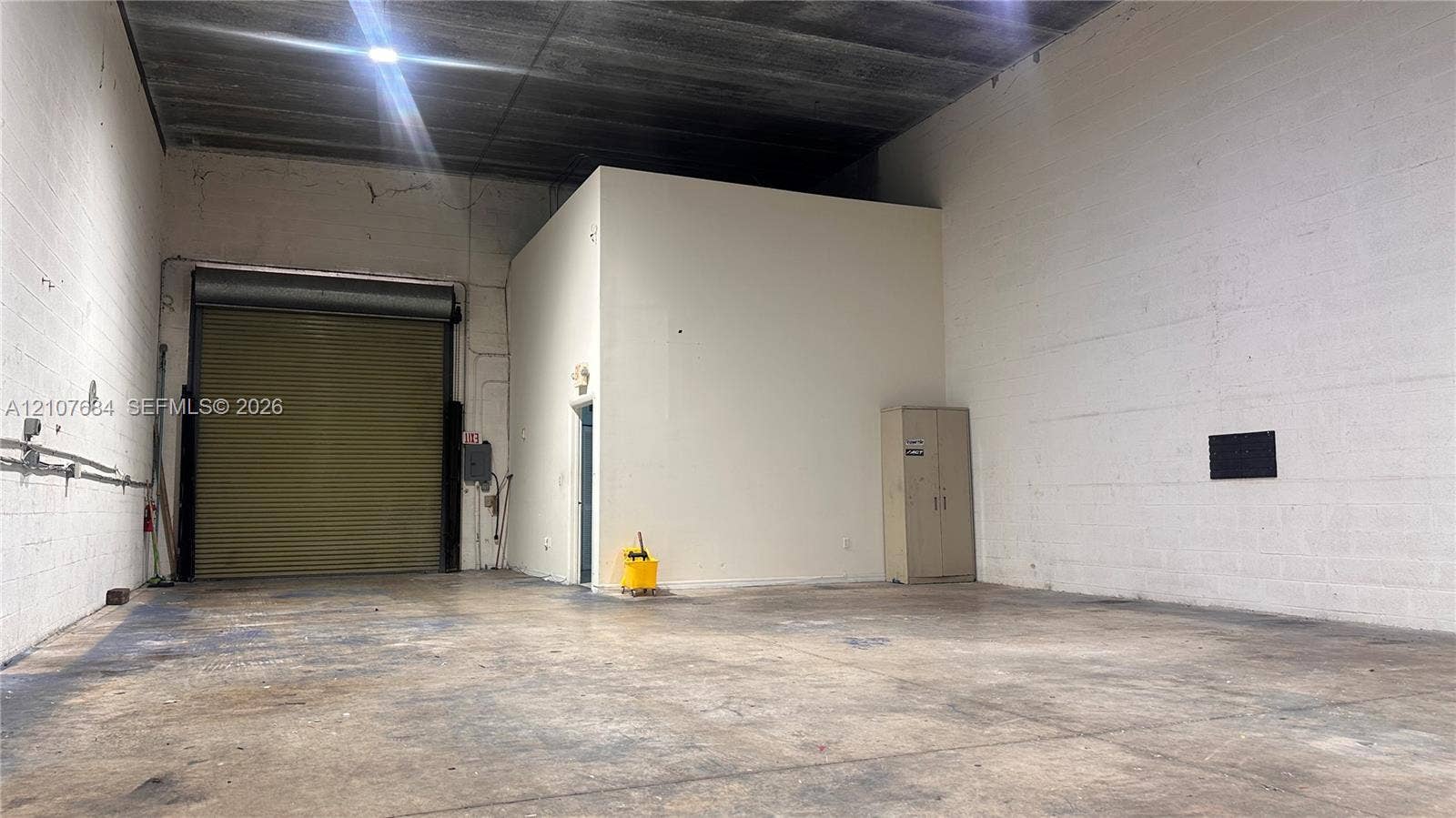 Industrial warehouse space featuring high ceilings, concrete flooring,, and a metal roll-up loading door