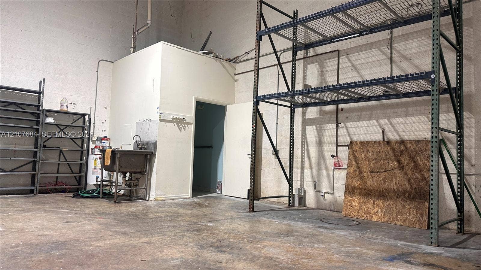 Industrial workspace featuring high ceilings, painted masonry walls, concrete flooring, integrated heavy-duty metal shelving units, and a stainless steel utility sink