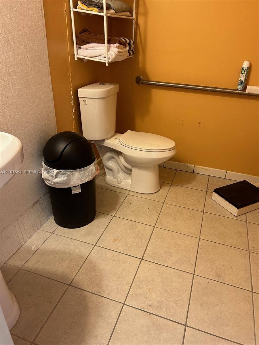 Ceramic tile flooring, white porcelain toilet, and wall-mounted metal support bar