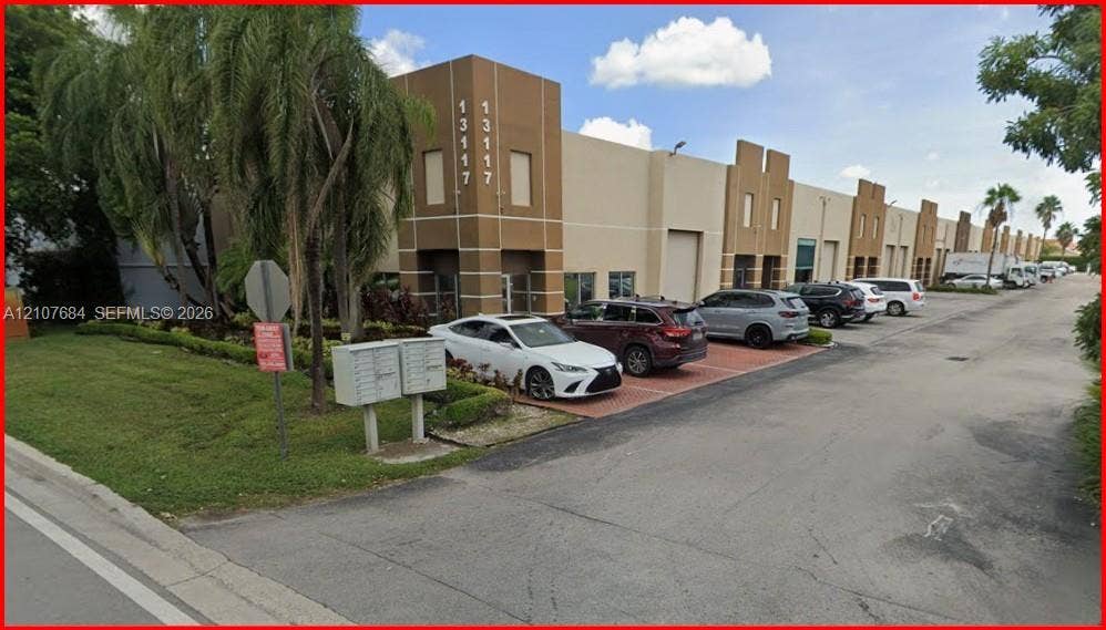 Commercial exterior featuring a concrete facade with decorative quoins, multiple ground-level roll-up doors, paved parking area, and manicured landscaping
