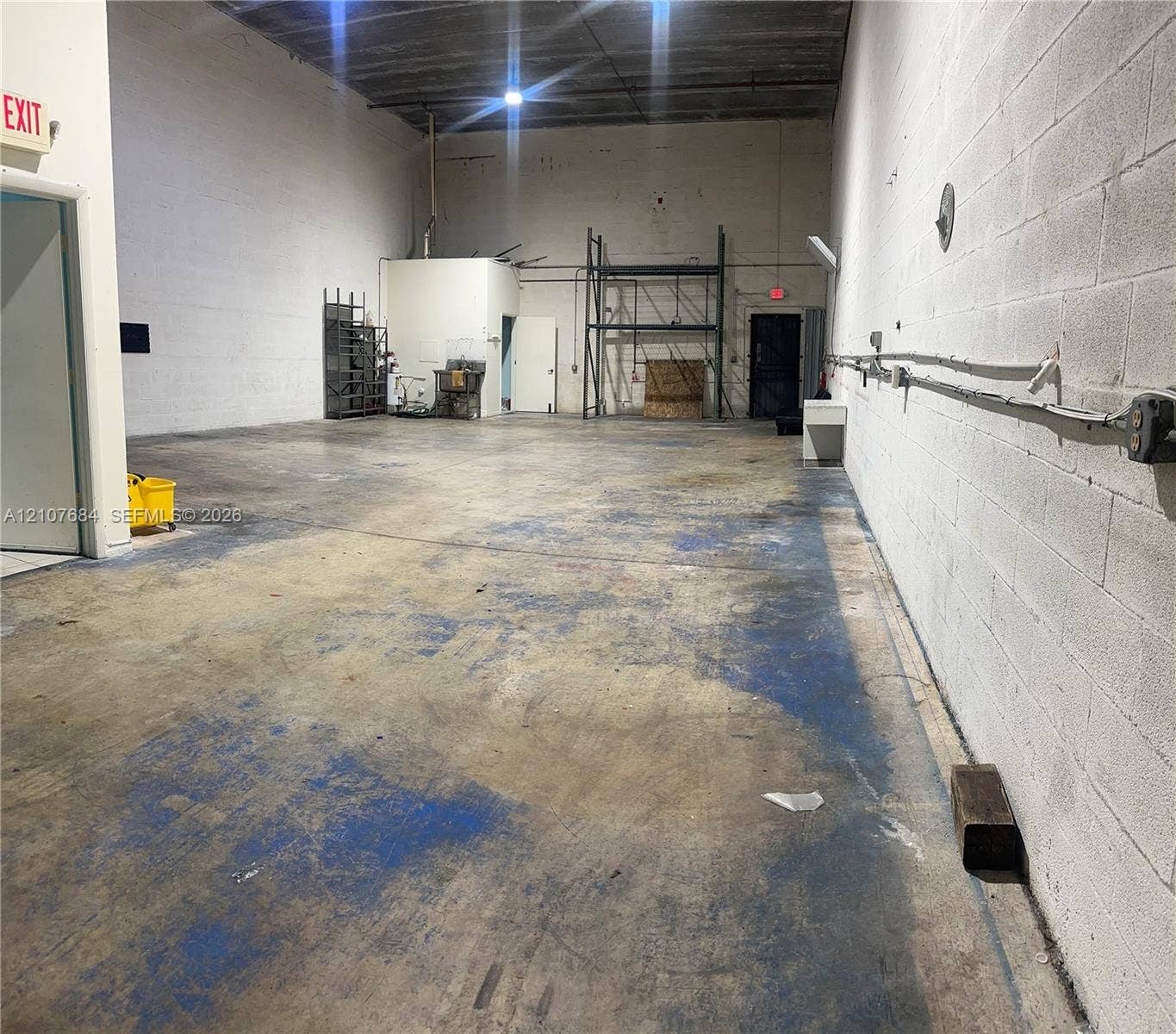 Industrial space featuring exposed concrete block walls, high ceilings, concrete flooring, and metal racking units
