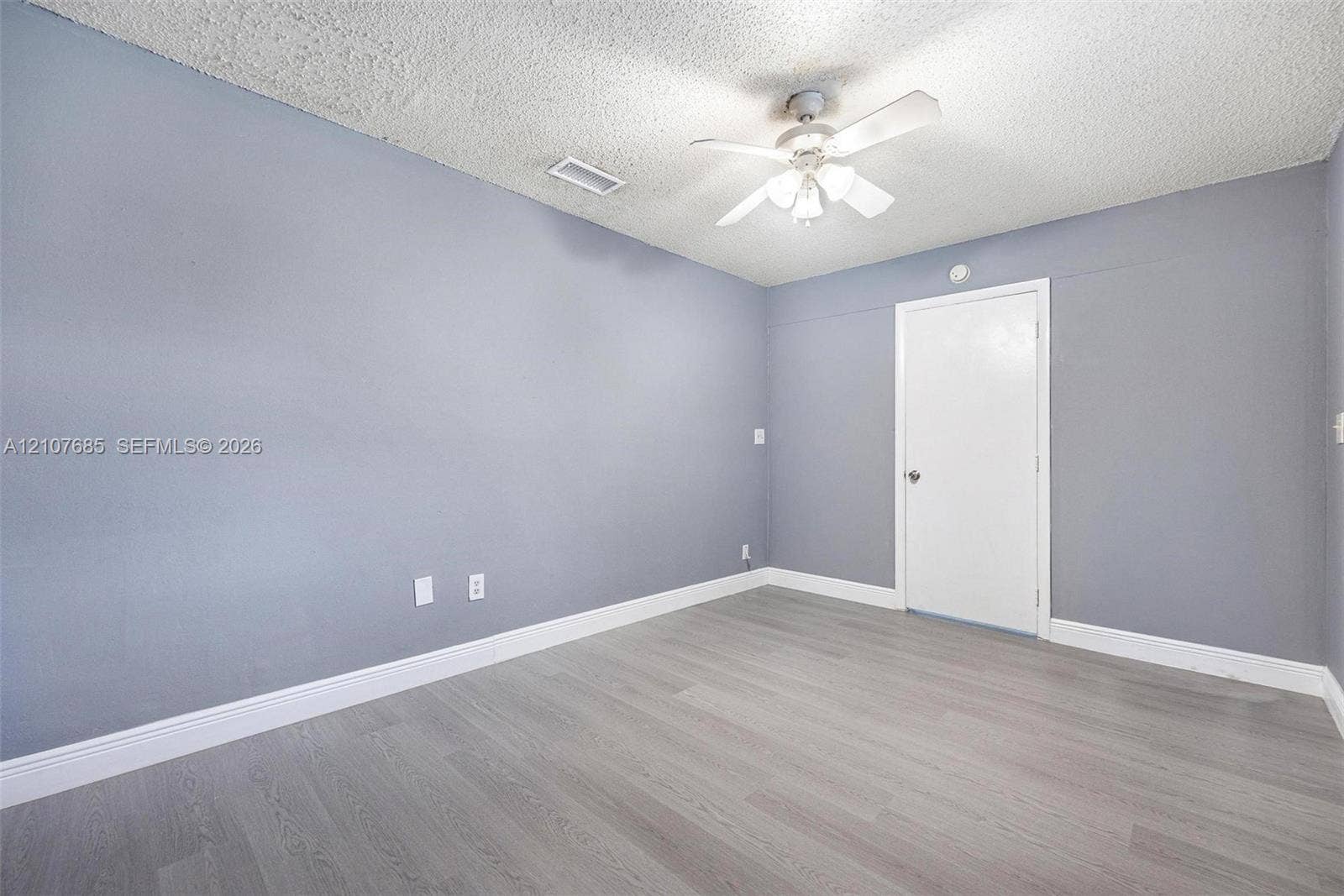 1460 Jefferson Drive, #1460L, Homestead, FL 33034 Neutral-toned interior room featuring wood-finish flooring, a ceiling-mounted light fixture with fan blades, and a solid-core interior door