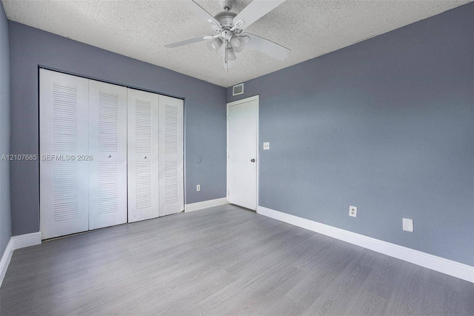 1460 Jefferson Drive, #1460L, Homestead, FL 33034 Room featuring wood-finish flooring, four-panel louvered closet doors, and a ceiling-mounted fan with integrated light fixture