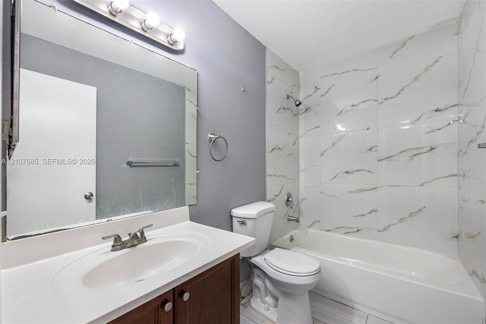 1460 Jefferson Drive, #1460L, Homestead, FL 33034 Bathroom featuring a vanity with an integrated sink, large wall-mounted mirror, light fixture with globe shades, and a shower-tub combination finished with floor-to-ceiling stone-look tile
