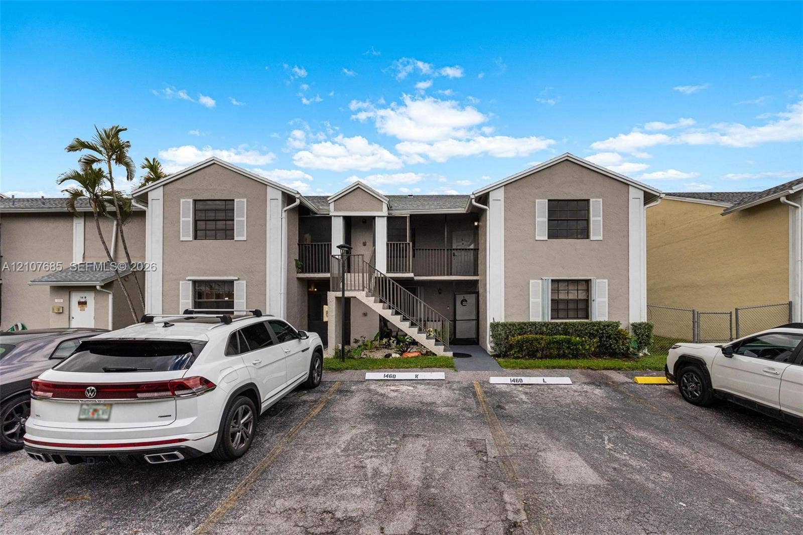 1460 Jefferson Drive, #1460L, Homestead, FL 33034 Two-story exterior featuring a neutral stucco facade, white trim accents, gabled rooflines, designated parking spaces, and covered entryways