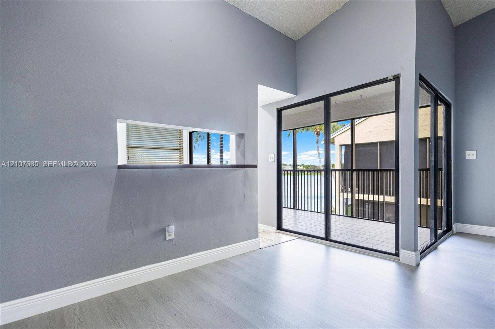 1460 Jefferson Drive, #1460L, Homestead, FL 33034 Vaulted ceilings, wood-finish flooring, interior pass-through window with ledge, and floor-to-ceiling sliding glass doors opening to a screened-in balcony