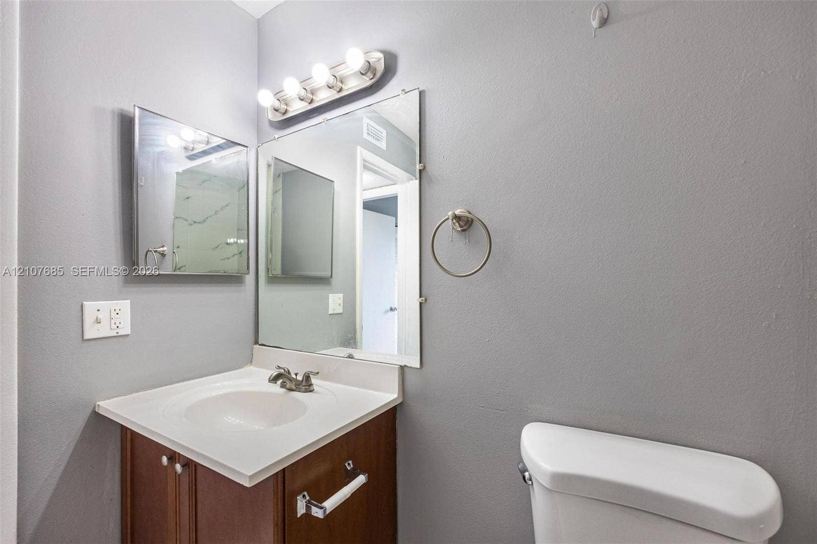 1460 Jefferson Drive, #1460L, Homestead, FL 33034 Vanity featuring a solid-surface integrated sink, wood-finish cabinetry, a large frameless mirror, and a four-light fixture