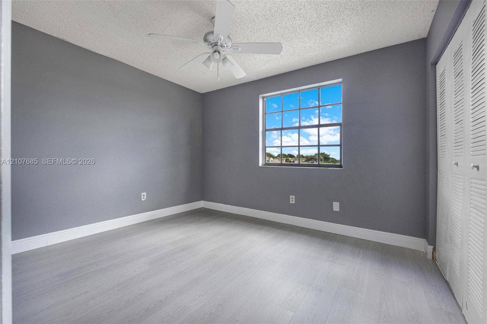 1460 Jefferson Drive, #1460L, Homestead, FL 33034 Room featuring gray walls, wood-finish flooring, a multi-pane window, a ceiling fan, and louvered bifold closet doors