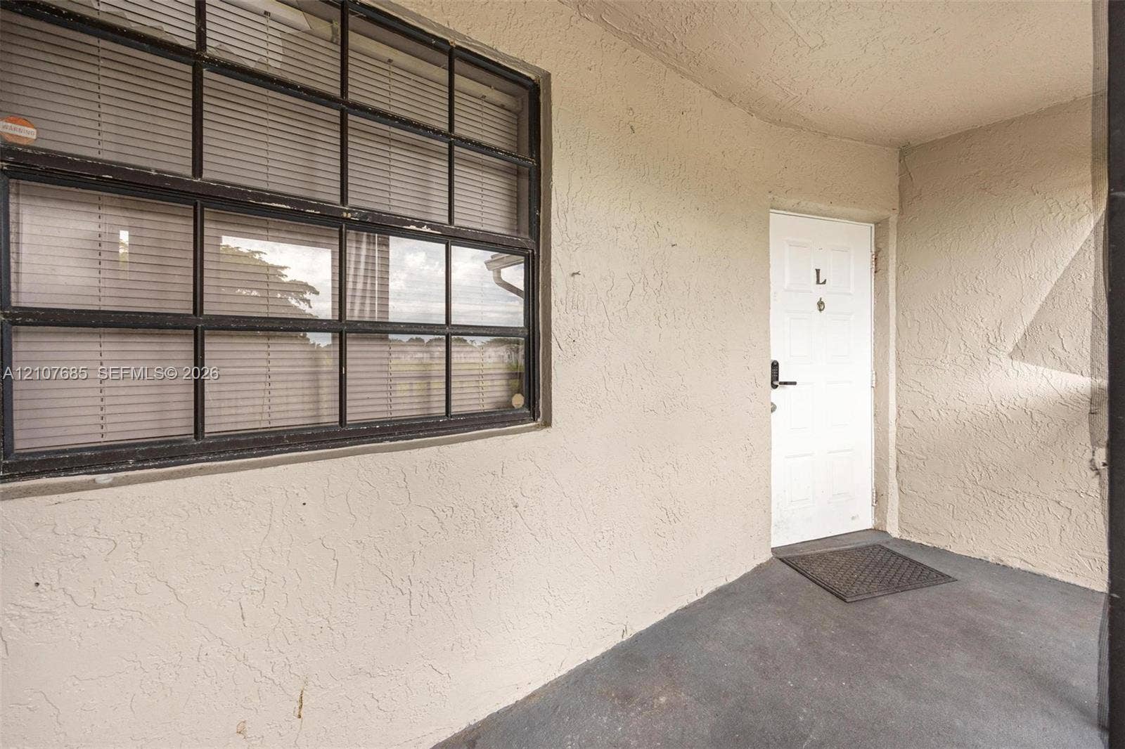 1460 Jefferson Drive, #1460L, Homestead, FL 33034 Covered entry featuring a textured stucco exterior, a single-pane glass door with a hardware lever, and a multi-lite window with a dark frame