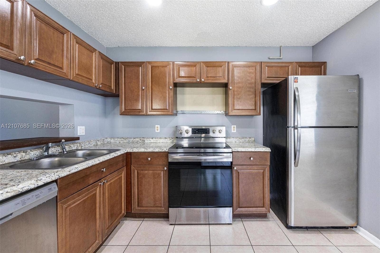 1460 Jefferson Drive, #1460L, Homestead, FL 33034 Kitchen featuring raised-panel wood cabinetry, stone-patterned countertops, stainless steel appliances, a double-basin stainless steel sink, and ceramic tile flooring