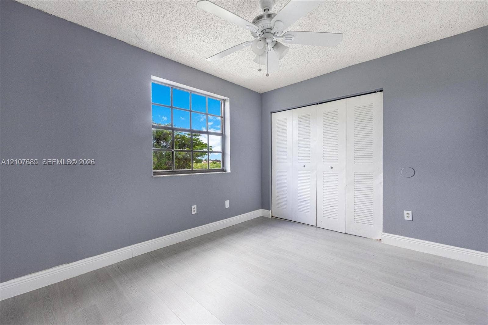 1460 Jefferson Drive, #1460L, Homestead, FL 33034 Room featuring wood-finish flooring, white louvered-style closet doors, a multi-pane window, and a ceiling fan