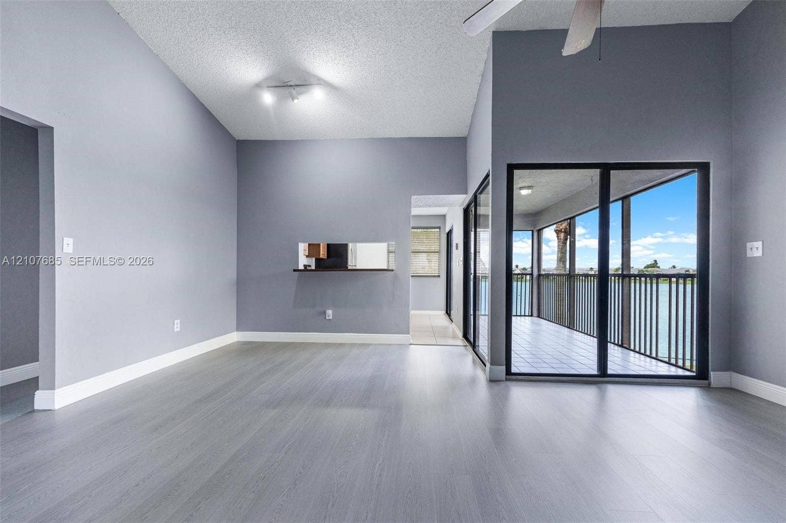 1460 Jefferson Drive, #1460L, Homestead, FL 33034 Vaulted ceilings featuring a ceiling fan, neutral wall paint, wood-finish flooring, a kitchen pass-through window, and floor-to-ceiling glass sliding doors opening to a covered balcony