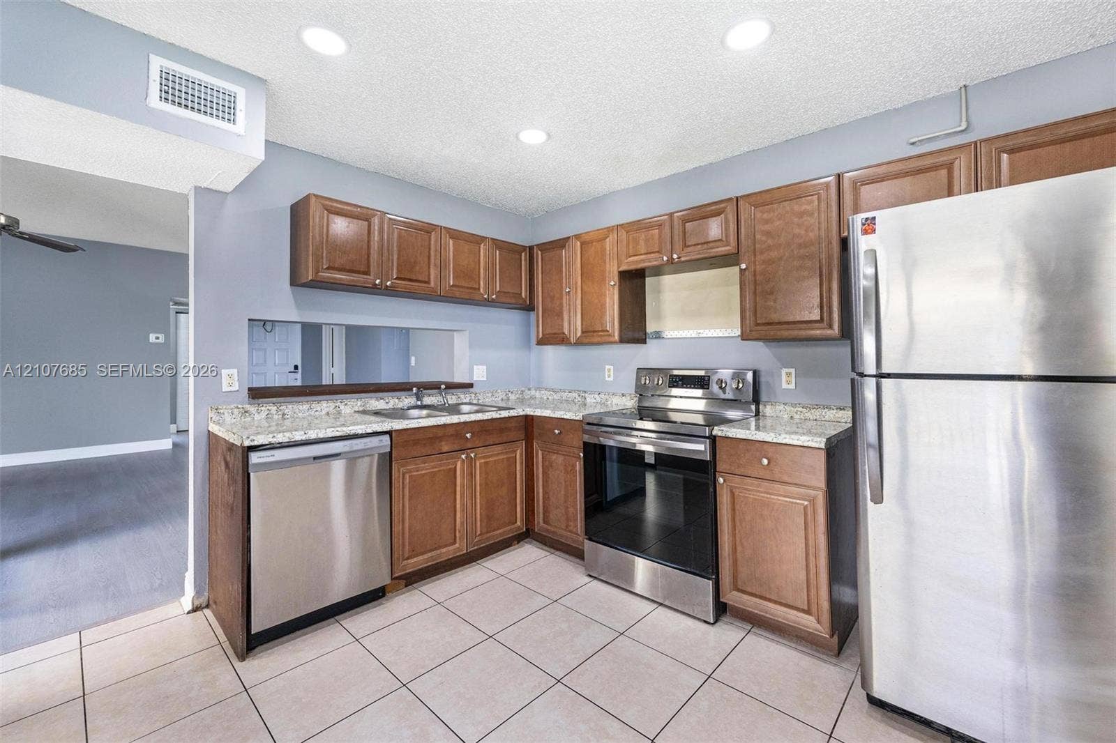1460 Jefferson Drive, #1460L, Homestead, FL 33034 Kitchen featuring medium-toned wood cabinetry, stone-finish countertops, stainless steel appliances, recessed ceiling lighting, and tile flooring