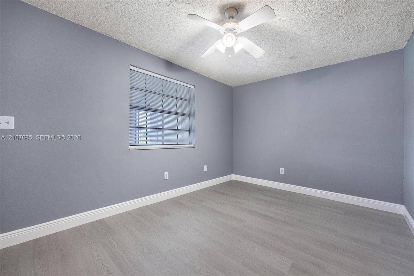 1460 Jefferson Drive, #1460L, Homestead, FL 33034 Room featuring wood-finish flooring, textured ceiling, light-toned wall paint, white-framed window with blinds, and a white ceiling fan with integrated light fixture