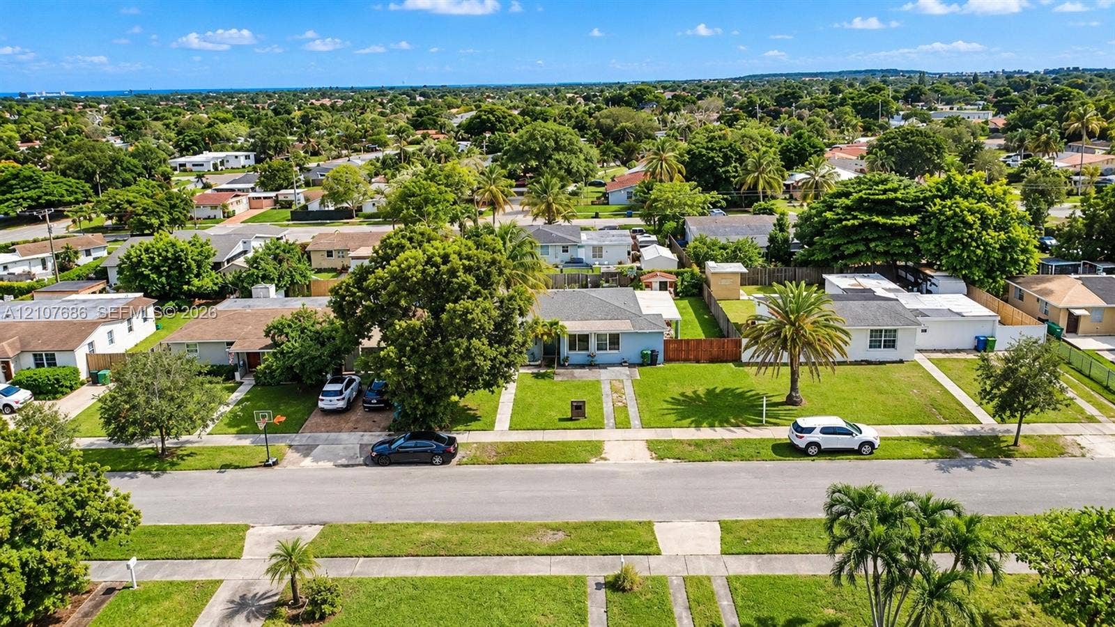 9760 Jamaica Drive, Cutler Bay, FL 33189 Aerial perspective of a single-story residence featuring a front lawn, mature canopy trees, a concrete driveway, and palm landscaping