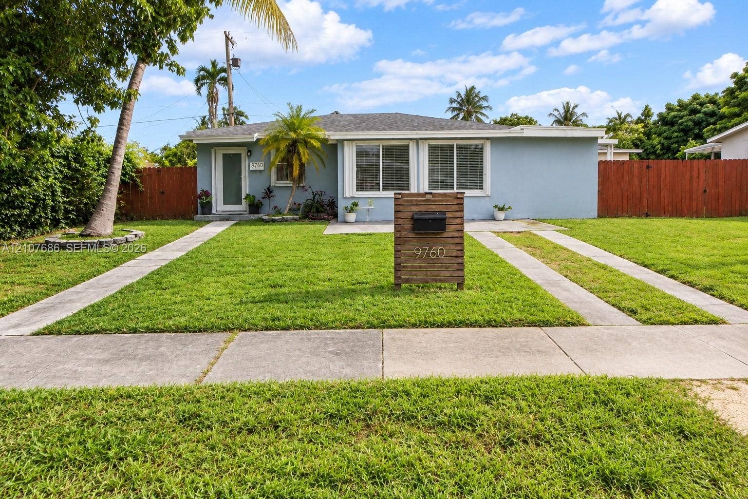 9760 Jamaica Drive, Cutler Bay, FL 33189 Single-story exterior featuring light-toned masonry, a horizontal wood-slat mailbox pedestal, dual-pane windows, and a paved concrete driveway