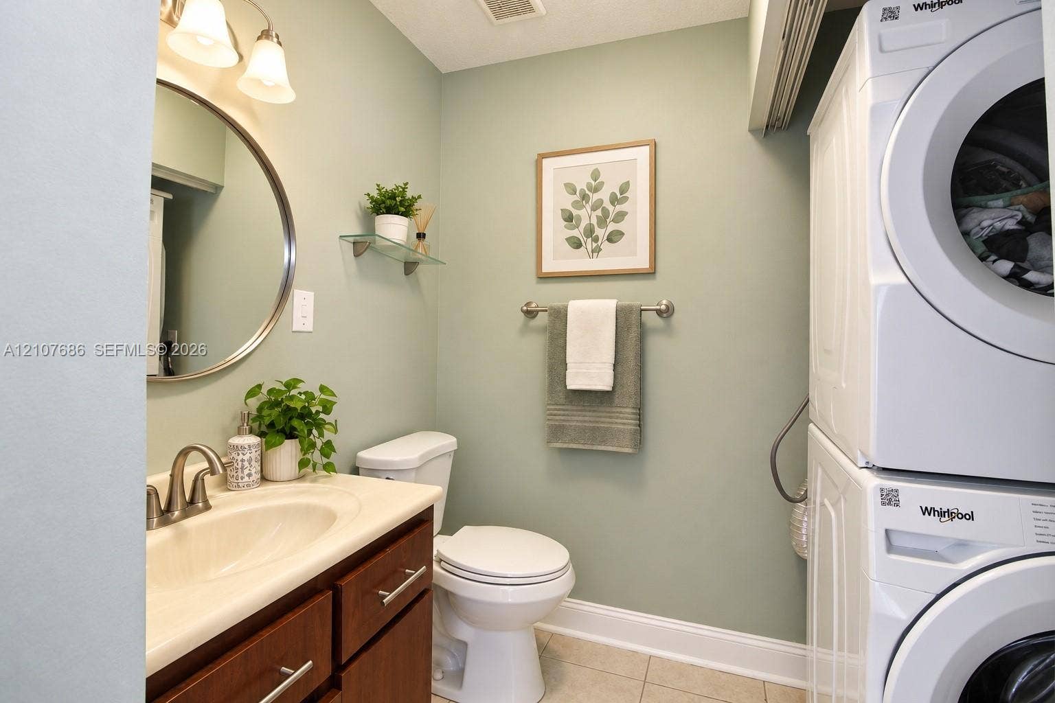 9760 Jamaica Drive, Cutler Bay, FL 33189 Laundry area featuring a stackable washer and dryer, wood-finish vanity with an integrated basin, circular wall mirror, and glass shelving