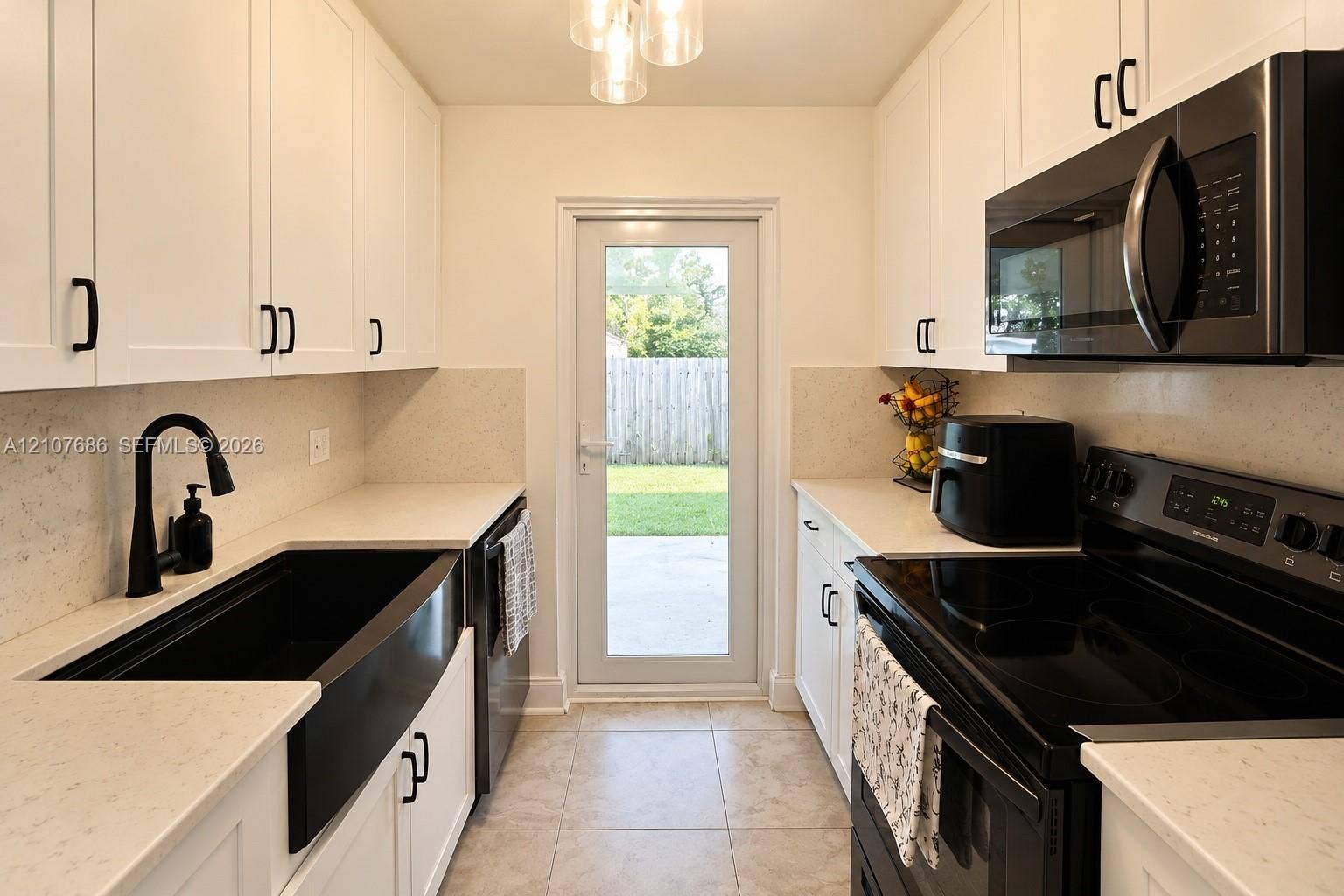 9760 Jamaica Drive, Cutler Bay, FL 33189 Kitchen featuring white shaker-style cabinetry, solid-surface countertops, a black farmhouse sink with a matching high-arc faucet, integrated black appliances, and tile flooring