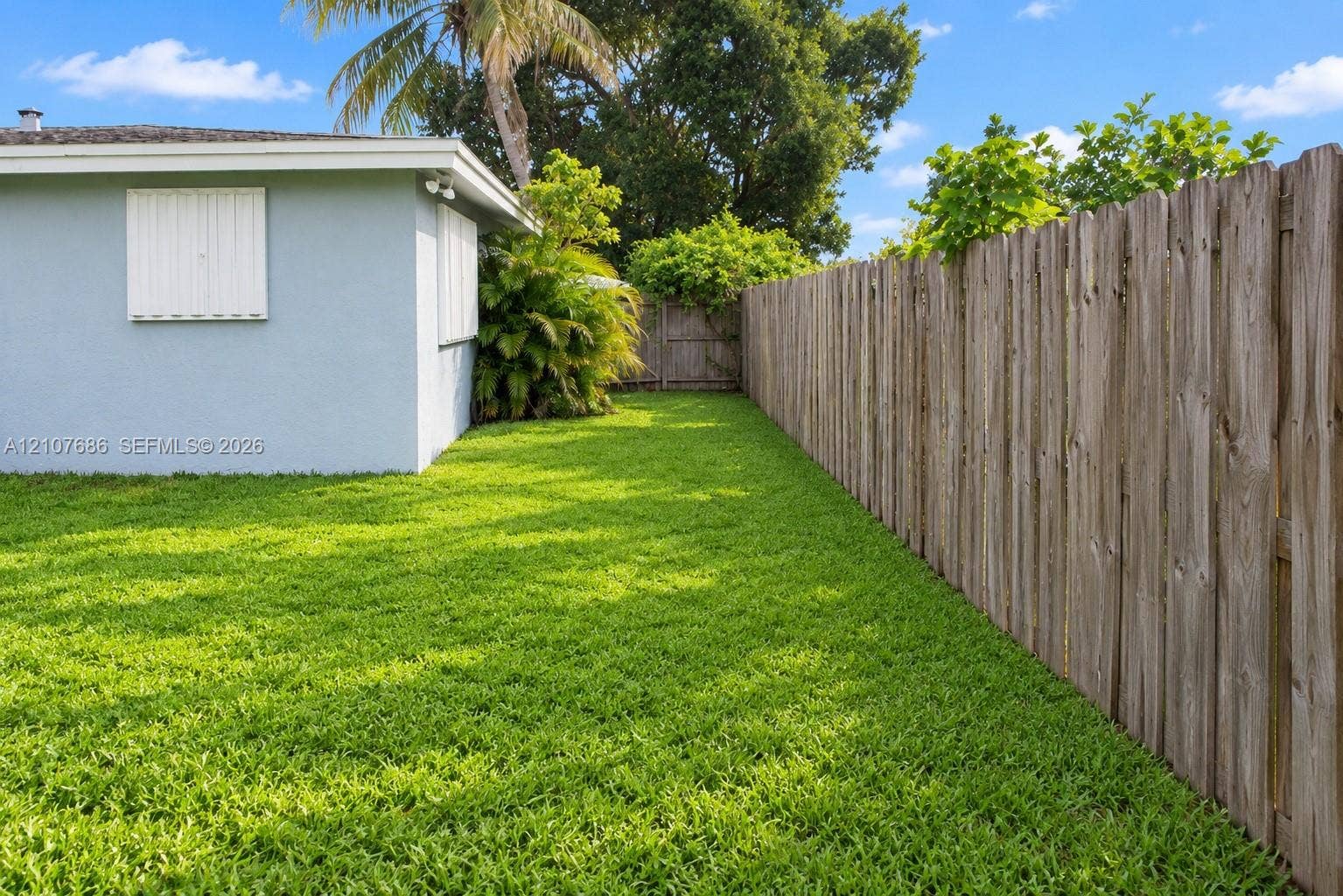 9760 Jamaica Drive, Cutler Bay, FL 33189 Private backyard featuring a manicured lawn, wood-panel fencing, exterior wall-mounted shutters, and mature landscaping