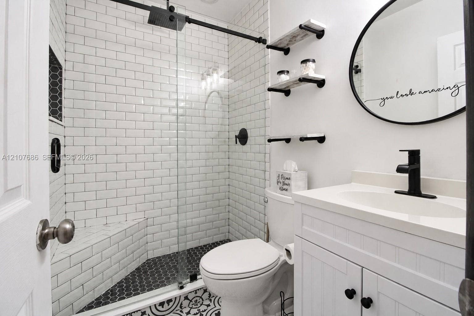 9760 Jamaica Drive, Cutler Bay, FL 33189 Bathroom featuring a glass-enclosed shower with white subway tile, hexagonal floor tiling, a white vanity with a single sink, matte black hardware, and wall-mounted shelving