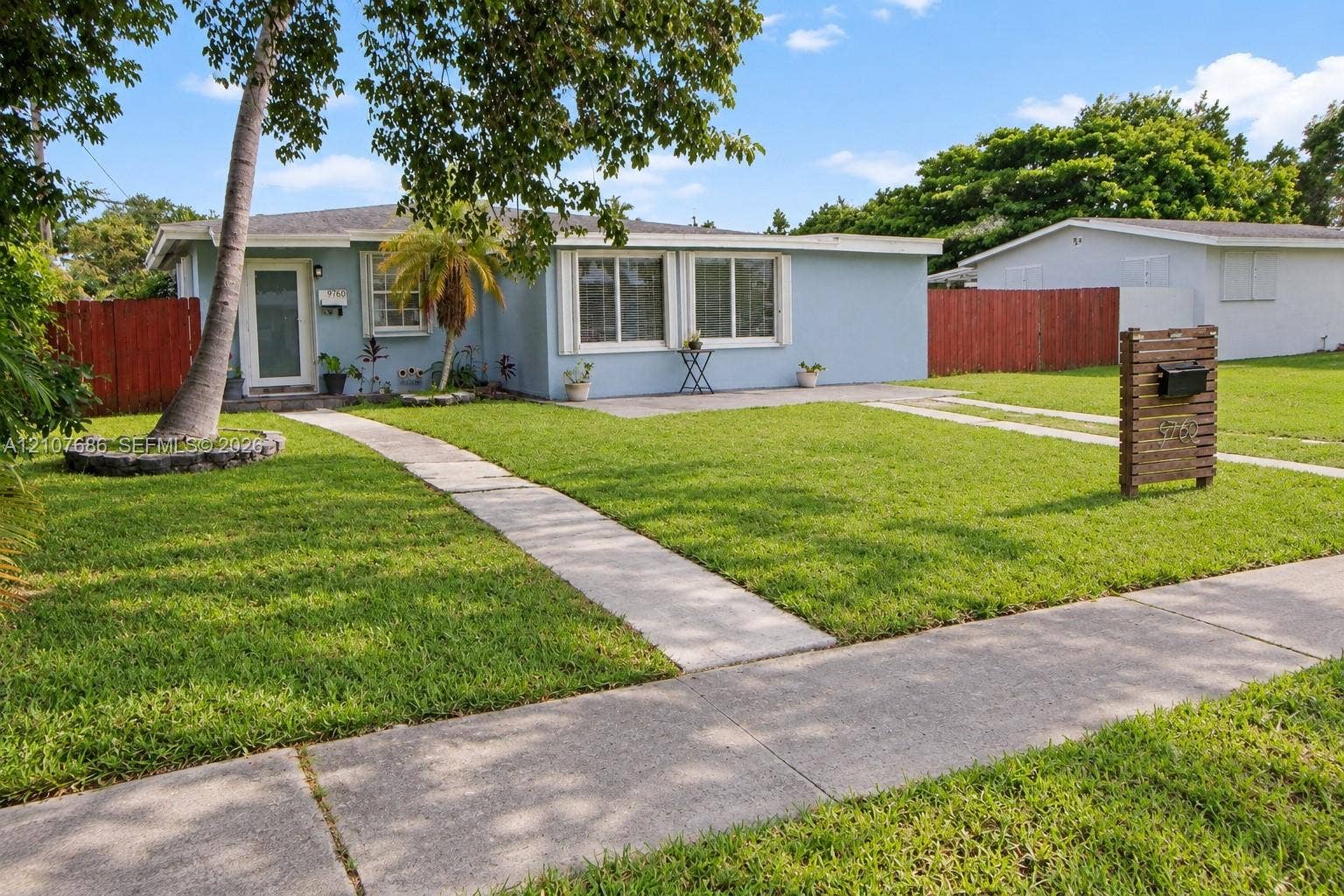 9760 Jamaica Drive, Cutler Bay, FL 33189 Single-story residence featuring a light-toned exterior, concrete walkway, horizontal wood-slat mailbox post, and perimeter privacy fencing