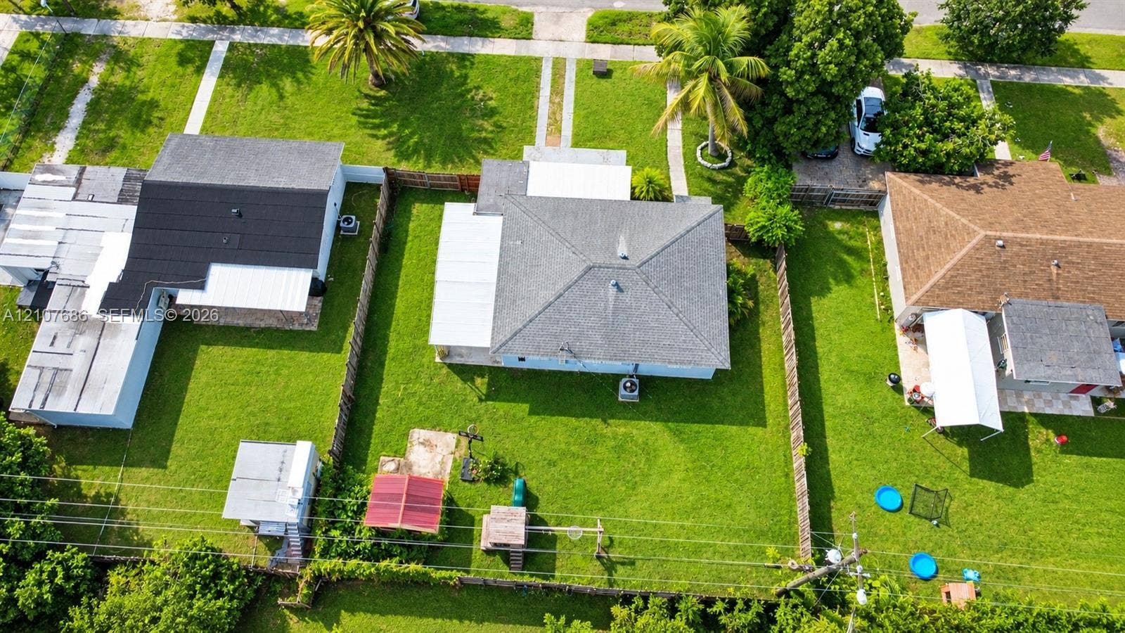 9760 Jamaica Drive, Cutler Bay, FL 33189 Aerial perspective of a detached residence featuring a hip roof, a concrete slab patio, a fenced backyard, and established perimeter greenery