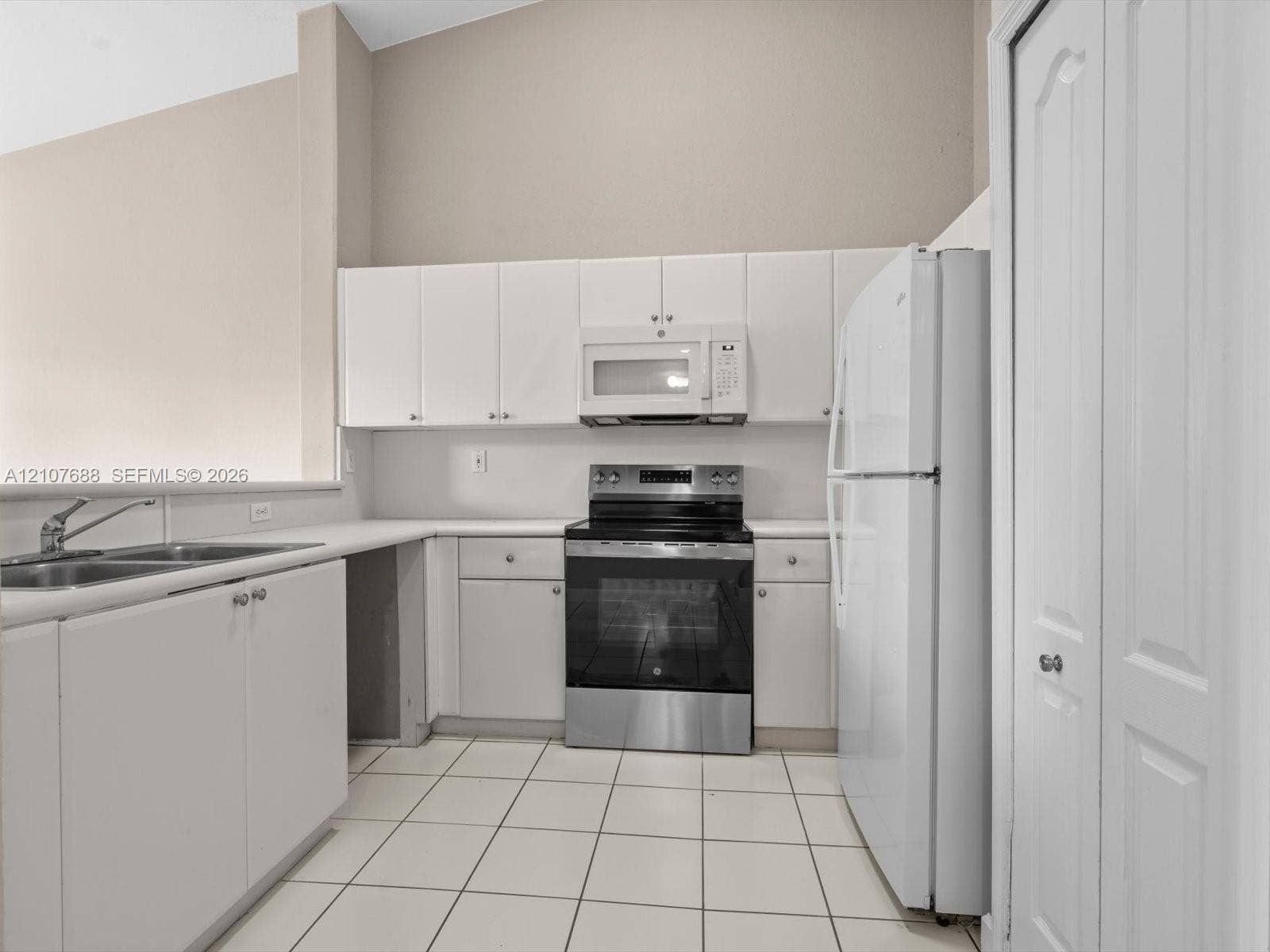 1677 SE 27th Court, #202, Homestead, FL 33035 Kitchen featuring white cabinetry, stainless steel oven, white tile flooring, double-basin sink, and vaulted ceiling