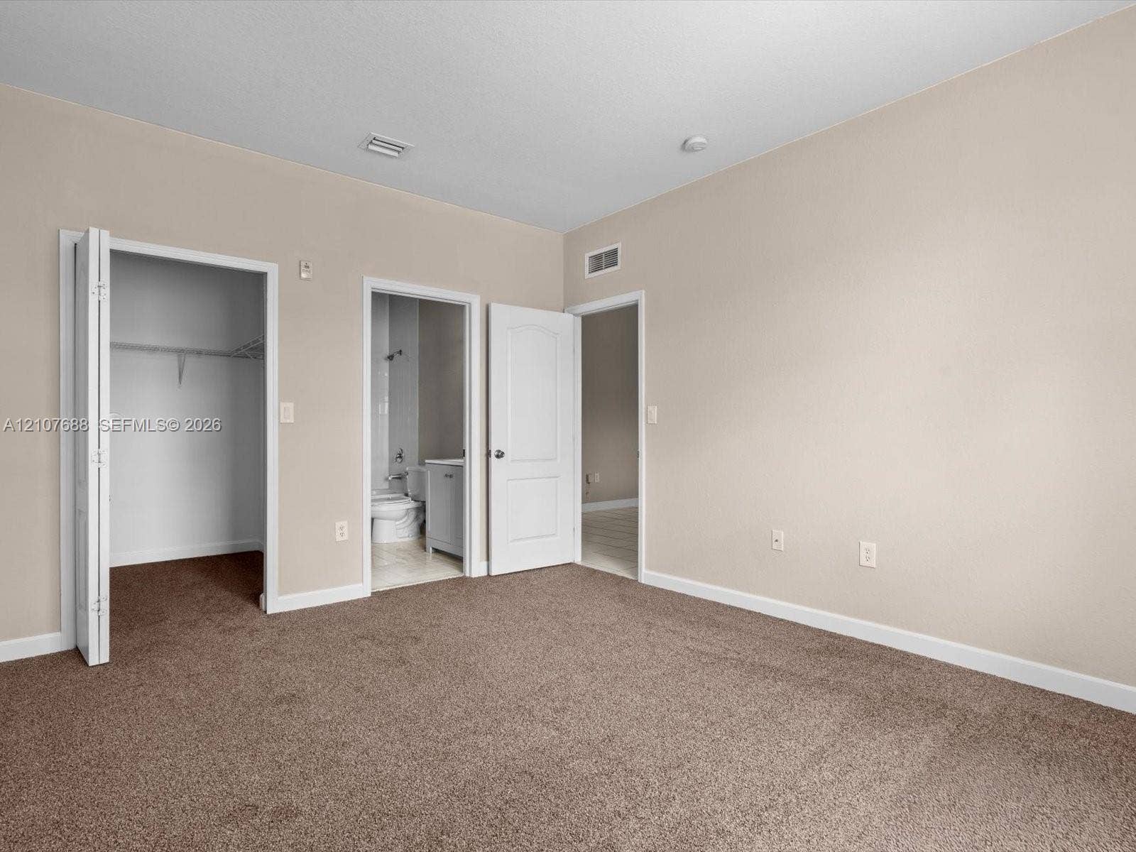 1677 SE 27th Court, #202, Homestead, FL 33035 Neutral-toned interior featuring wall-to-wall carpeting, multiple interior doorways, a built-in reach-in closet with shelving, and a separate doorway to a tiled bathroom