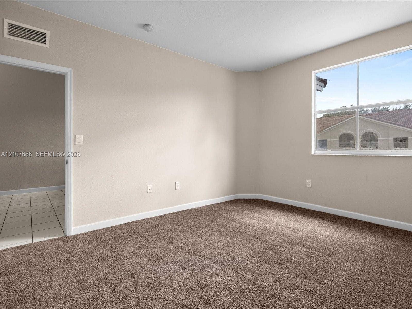 1677 SE 27th Court, #202, Homestead, FL 33035 Neutral-toned interior room featuring wall-to-wall carpeting, a single-pane window, and an arched-top doorway leading to a tiled-floor area