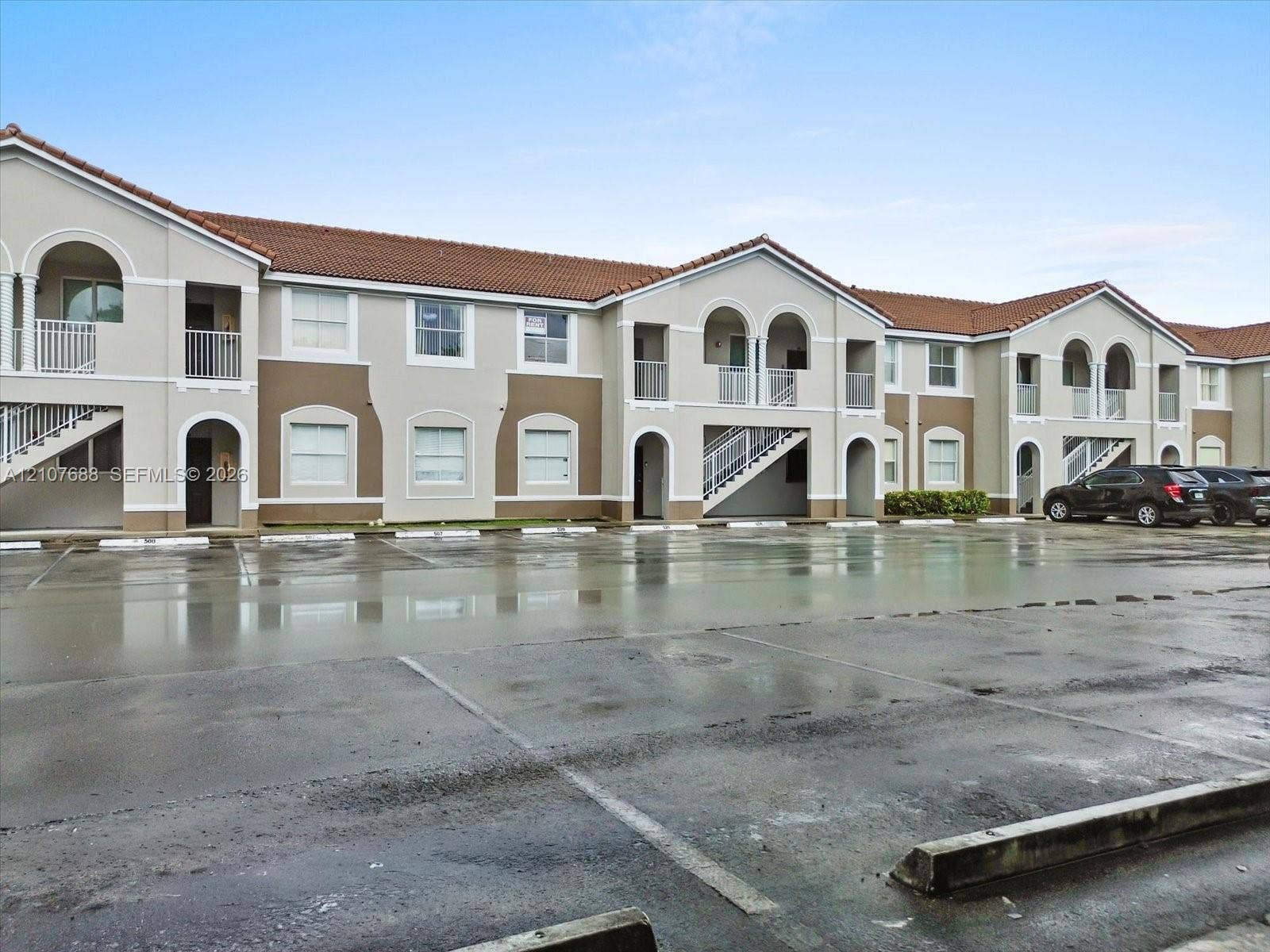 1677 SE 27th Court, #202, Homestead, FL 33035 Multi-story exterior featuring a tile roof, stucco facade, arched architectural details, and private balconies with metal railings