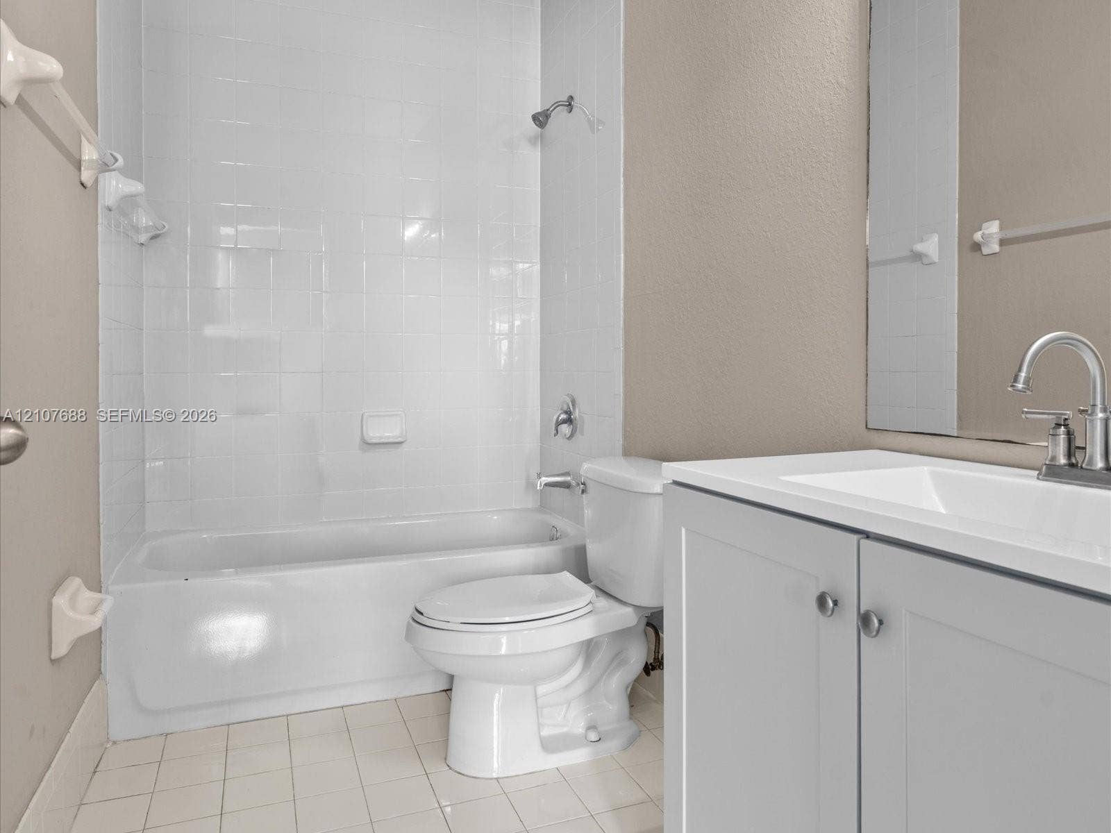 1677 SE 27th Court, #202, Homestead, FL 33035 Bathroom featuring a white porcelain tub with tiled surround, a vanity with a white countertop and basin, chrome faucet hardware, and tile flooring