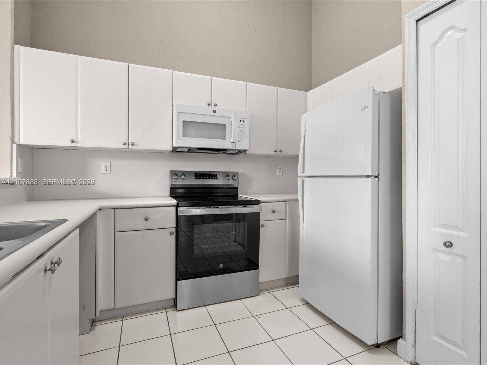 1677 SE 27th Court, #202, Homestead, FL 33035 Kitchen featuring white cabinetry, solid-surface countertops, stainless steel range with overhead microwave, white refrigerator, and tile flooring