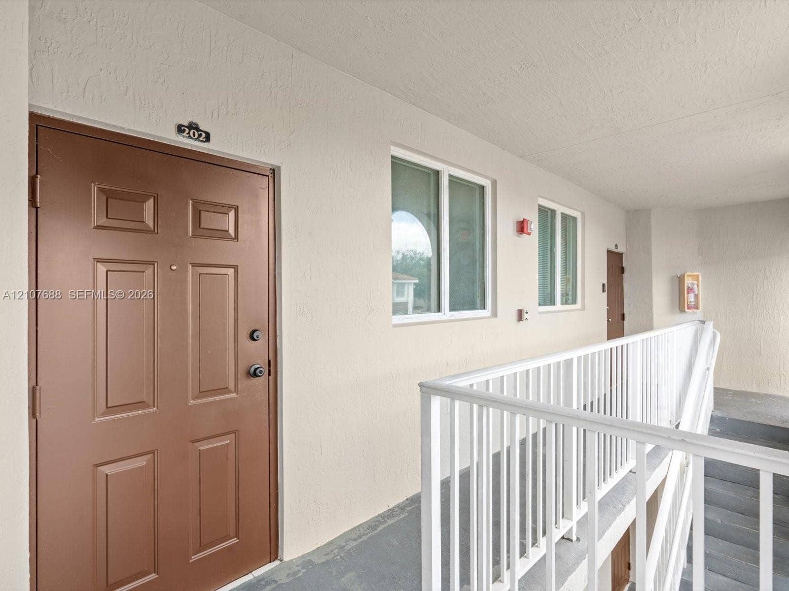 1677 SE 27th Court, #202, Homestead, FL 33035 Paneled entry door with hardware, neutral exterior wall finish, white metal railing, and dual-pane windows