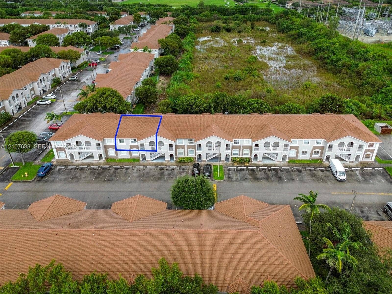1677 SE 27th Court, #202, Homestead, FL 33035 Multi-story building with a terracotta-toned tile roof and arched architectural detailing, featuring dedicated asphalt parking and professional landscaping