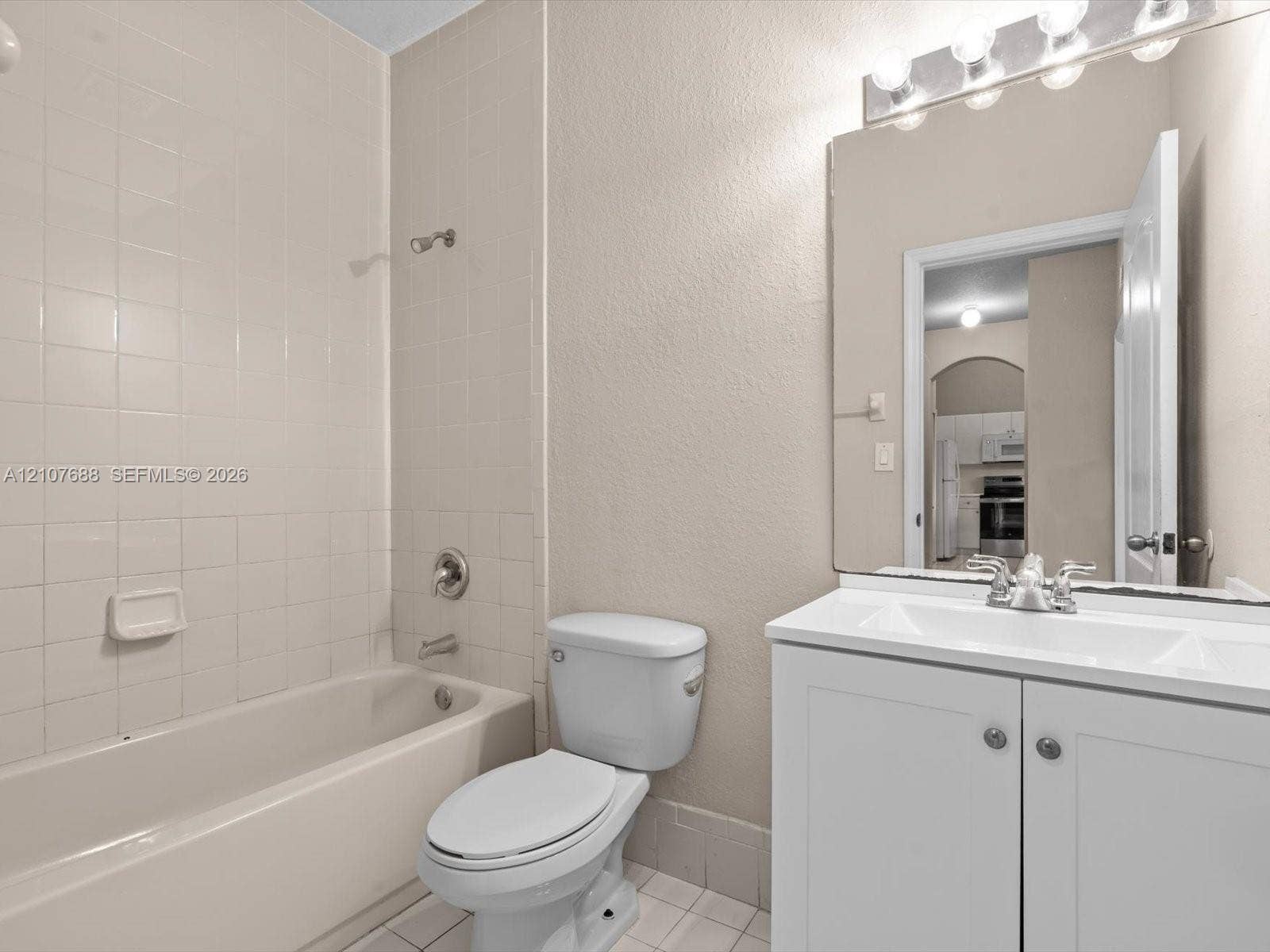 1677 SE 27th Court, #202, Homestead, FL 33035 Bathroom featuring a white vanity cabinet with a integrated sink, expansive wall-mounted mirror, multi-bulb vanity light, and a tiled shower surround