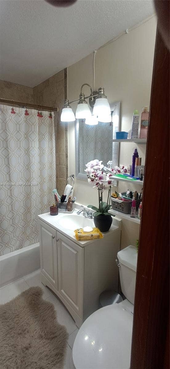 Bathroom vanity with white cabinetry, integrated sink, and polished metal faucet, complemented by a tri-light fixture above a framed mirror and wall-mounted shelving